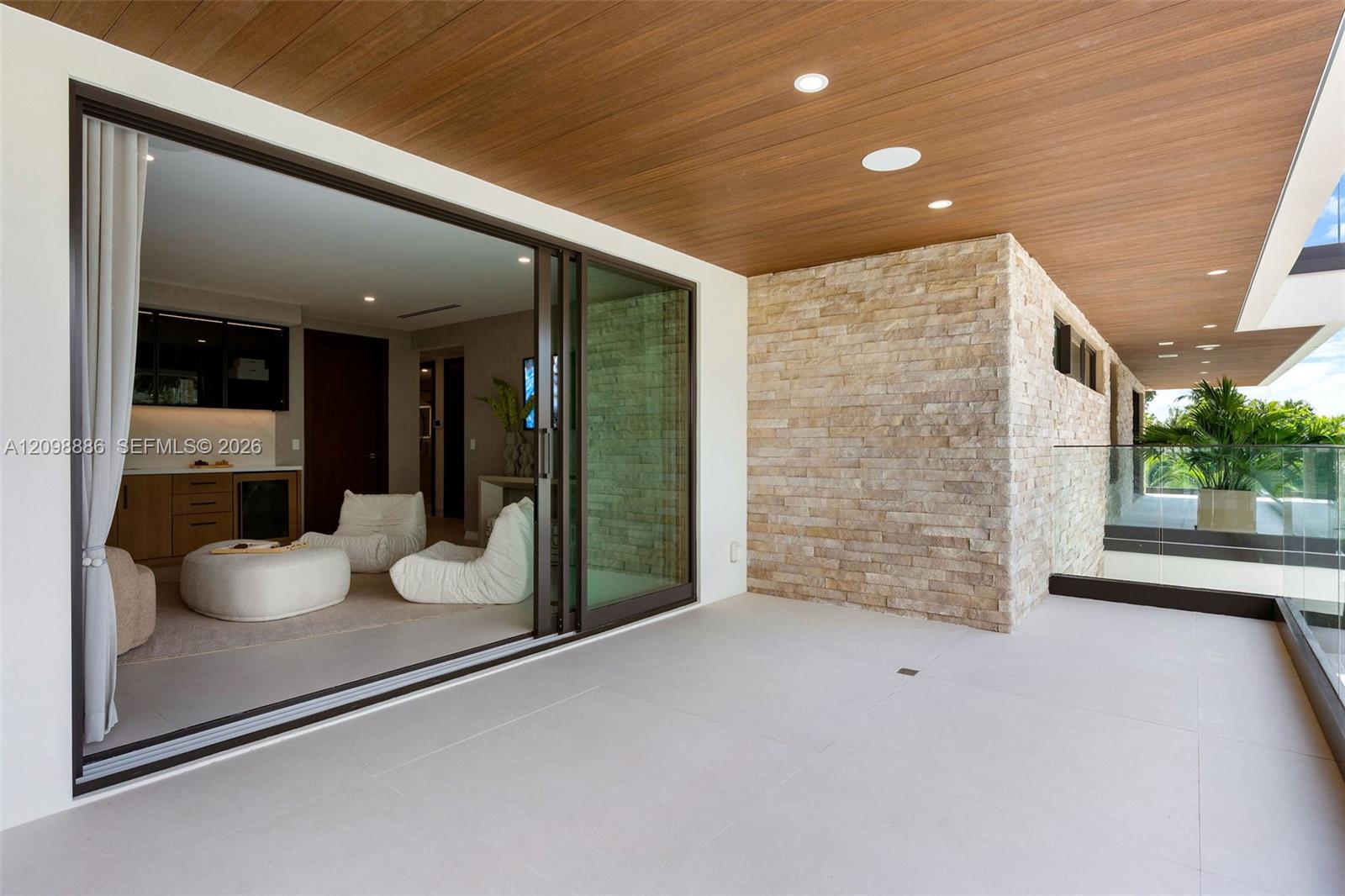 Covered balcony featuring wood-plank ceiling, large-format tile flooring, stacked-stone accent wall, recessed lighting, and expansive glass sliding doors