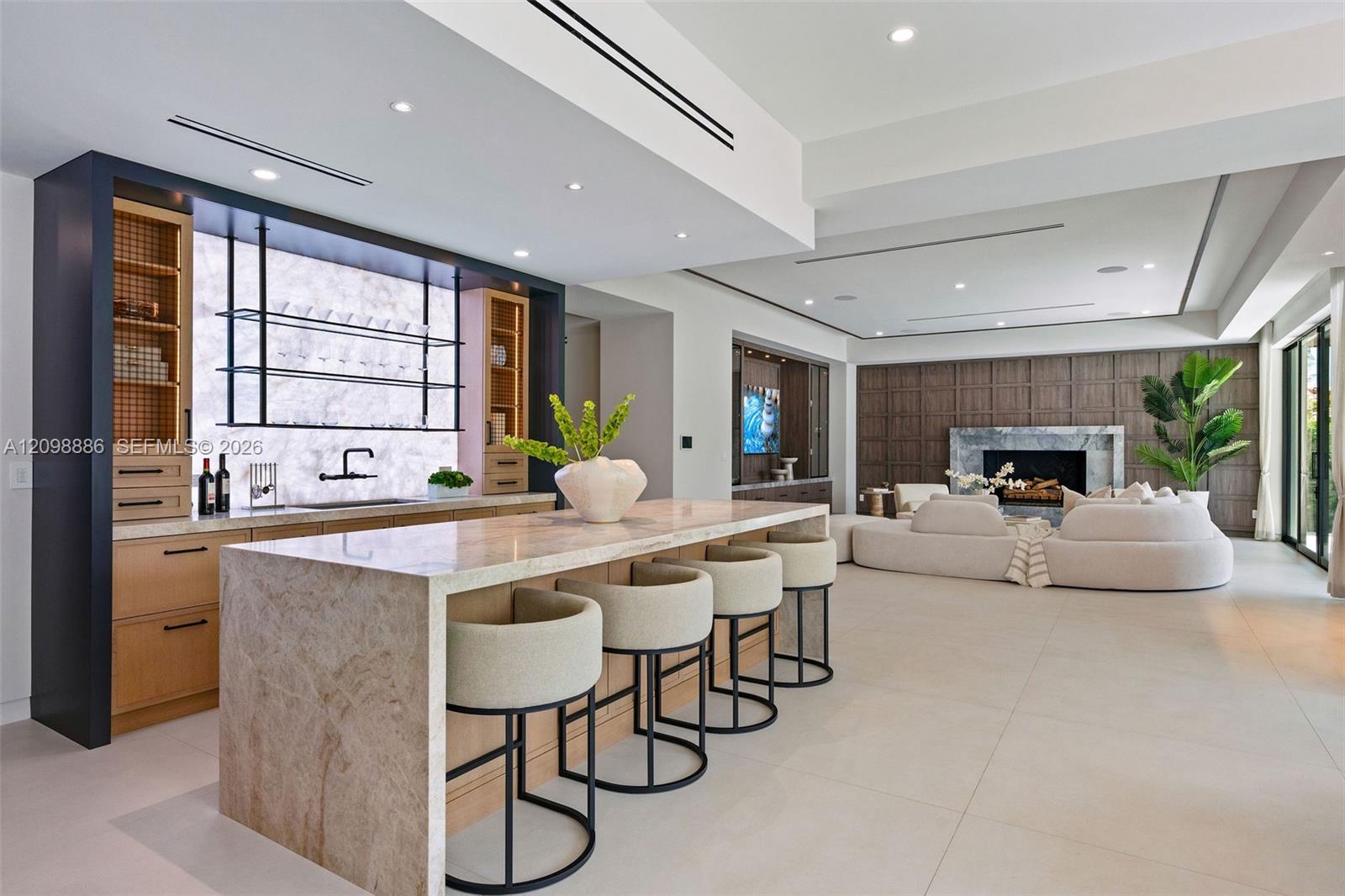 Stone-topped kitchen island with bar seating, custom cabinetry featuring integrated shelving, recessed lighting, and floor-to-ceiling wood wall paneling with an inset fireplace