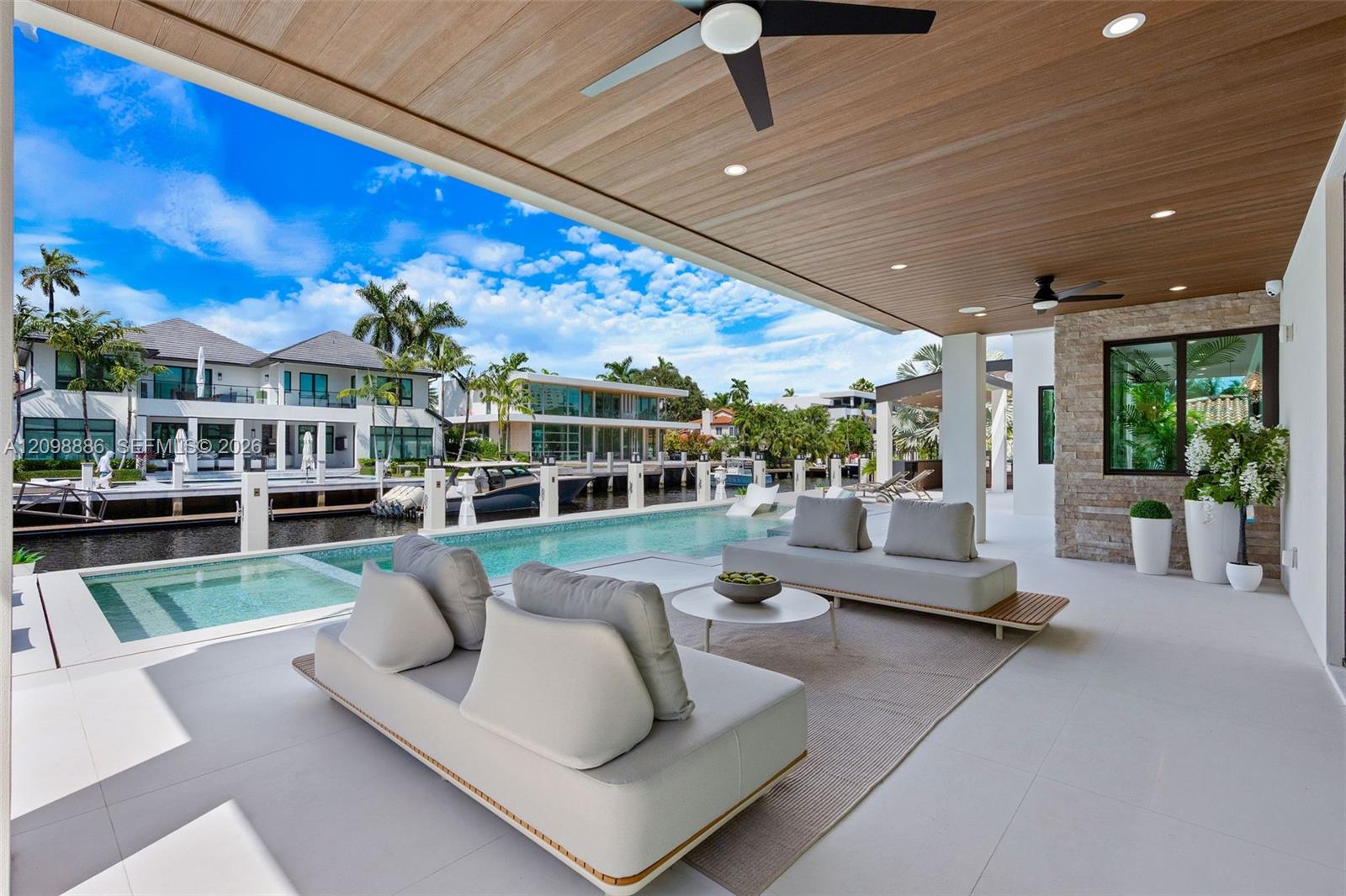 Covered patio featuring a wood-plank ceiling, recessed lighting, and dual ceiling fans, complete with a stone-accented wall and a custom pool bordering the canal