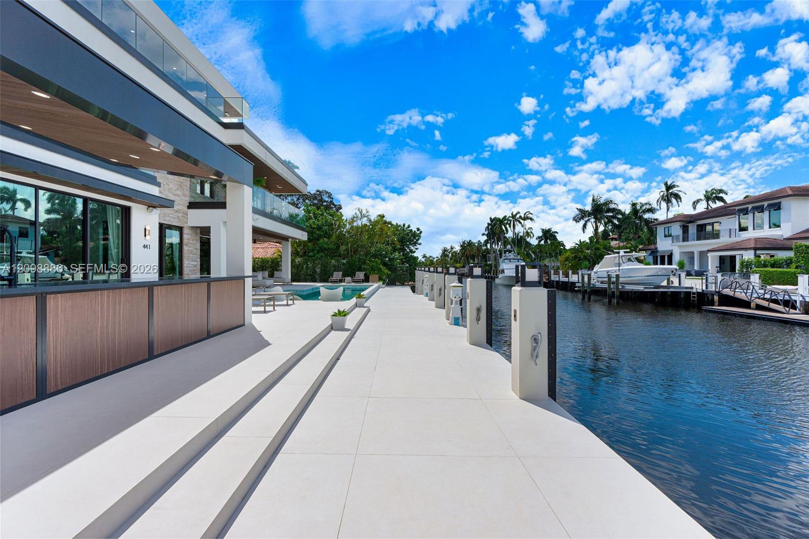 Waterfront terrace featuring large-format stone pavers, a built-in outdoor bar with wood-finish paneling, a swimming pool, and a private dock