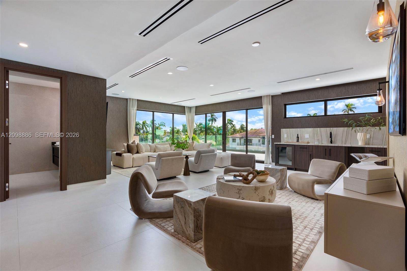 Large-format tile flooring, recessed linear lighting, floor-to-ceiling glass sliding doors, built-in wet bar with stone backsplash, and dark textured wall treatments