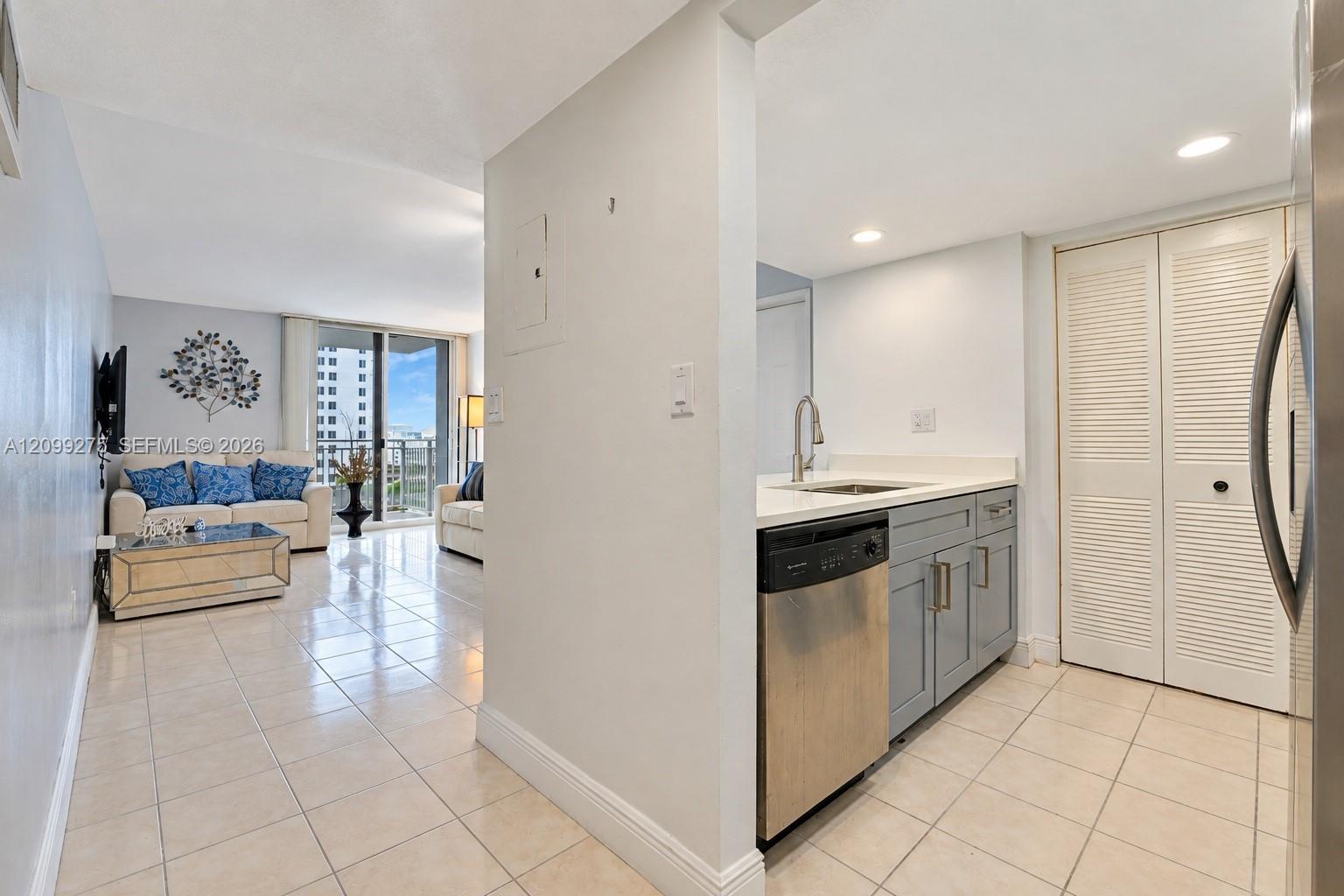 Modern galley kitchen featuring gray cabinetry, white countertops, stainless steel appliances, a double-basin sink, and tile flooring.
