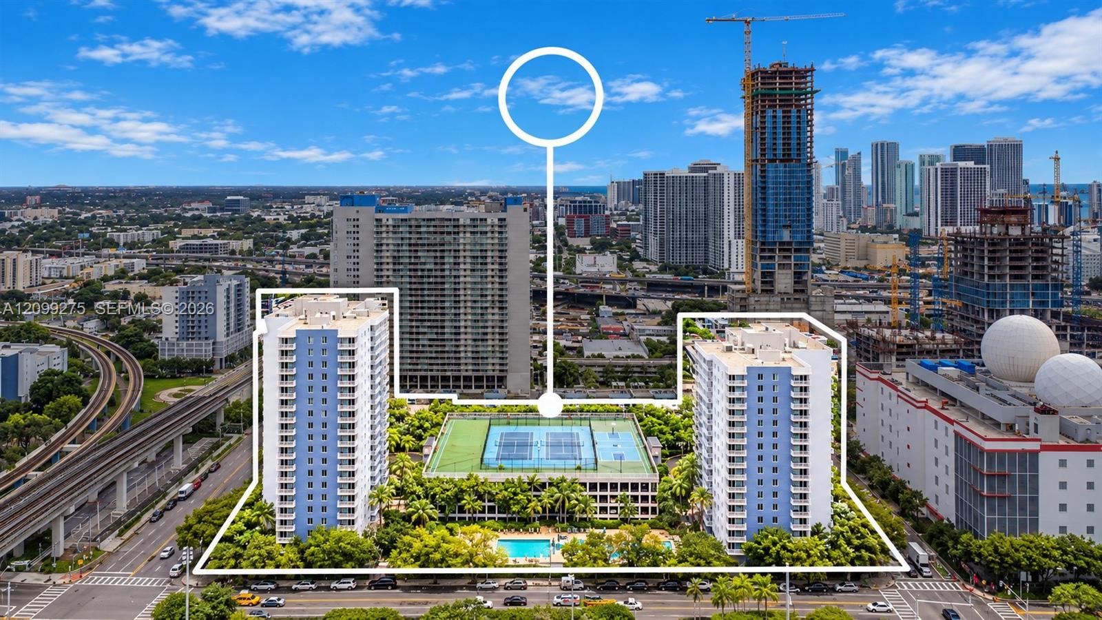 Aerial view highlighting the condominium complex, featuring two residential towers, sports court, a swimming pool, and lush landscaped grounds, set against the vibrant Miami downtown skyline. The white outline emphasizes the property boundaries and its amenities.