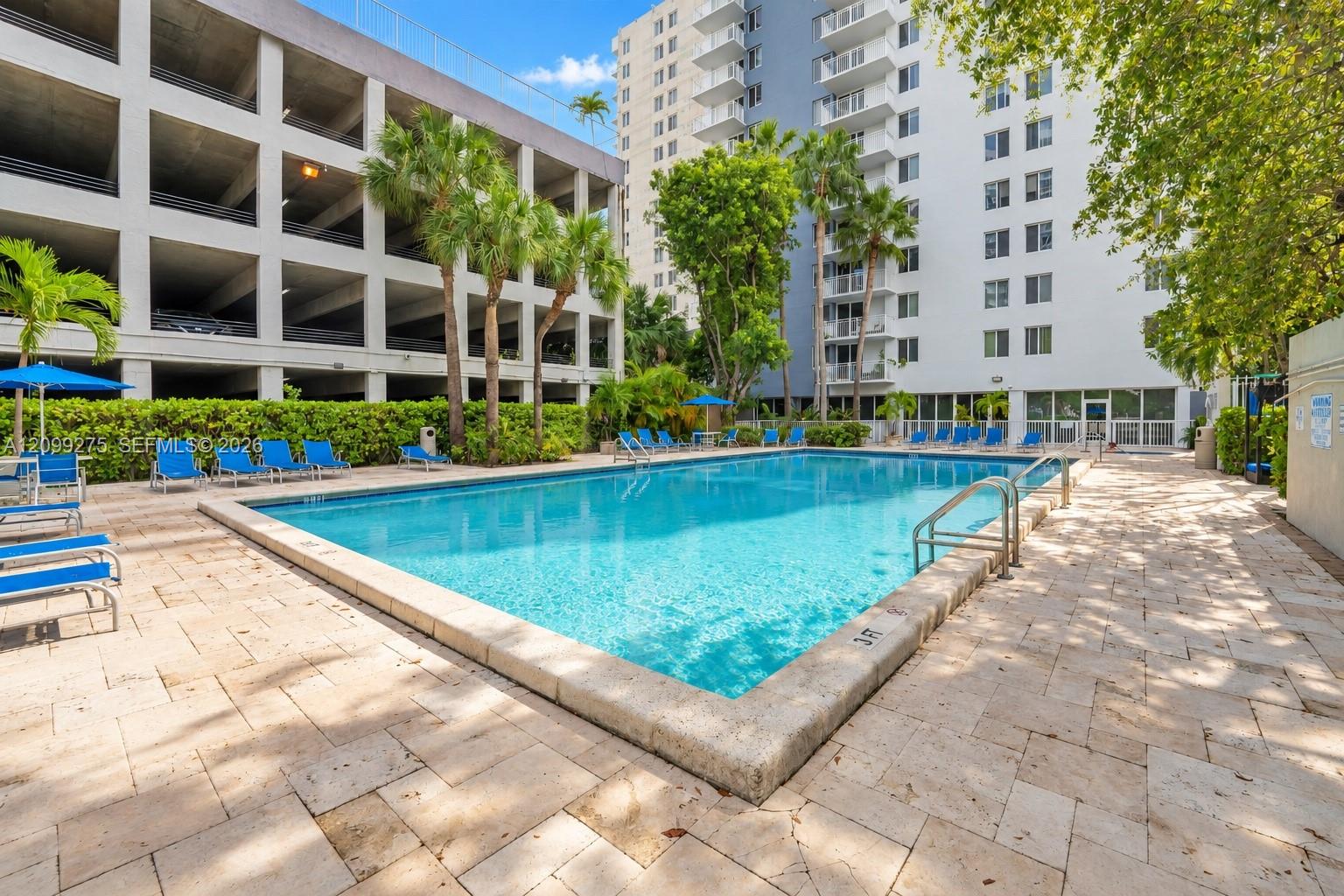 Resort-style swimming pool surrounded by tropical landscaping, spacious sun loungers, and a paved deck, offering residents a relaxing outdoor retreat.