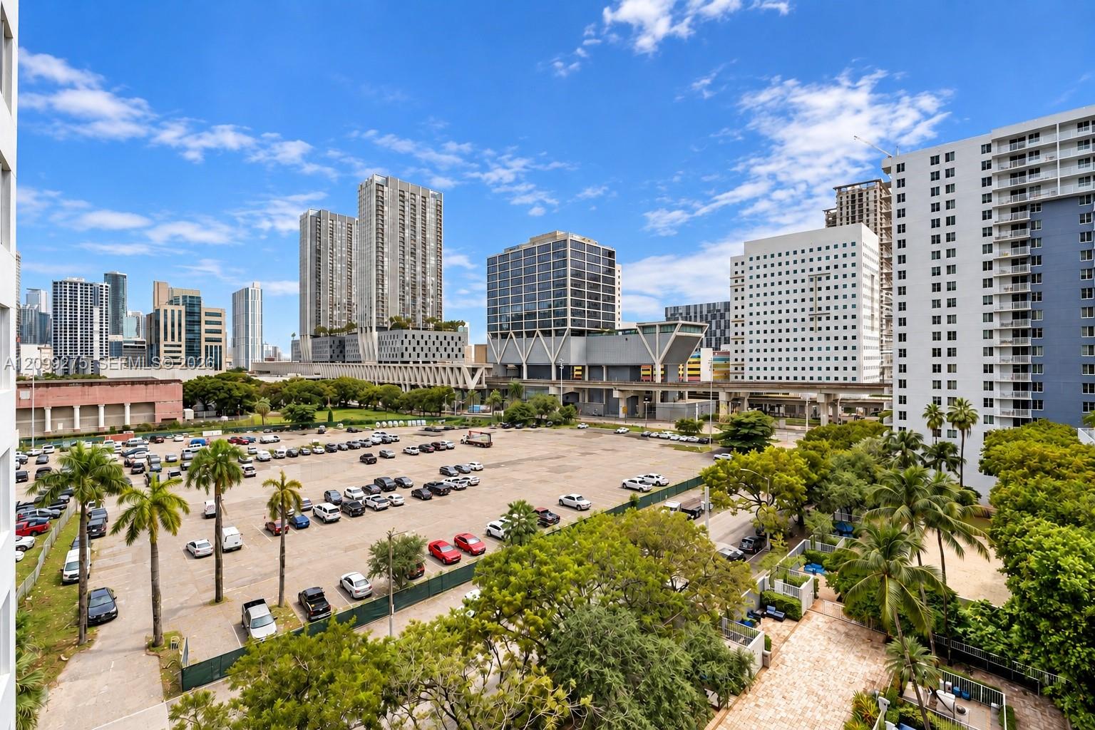 Panoramic city views featuring a vibrant downtown skyline, high-rise buildings, and a spacious parking area, complemented by lush tropical greenery and palm trees.
