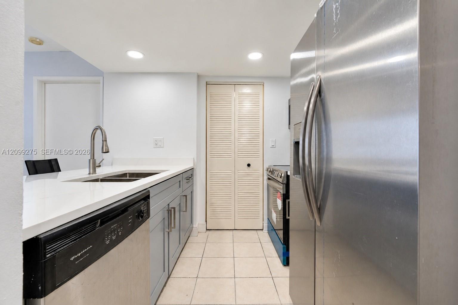 Bright kitchen and entryway featuring a breakfast bar with two stools, white countertops, stainless steel appliances, recessed lighting, and tiled flooring.