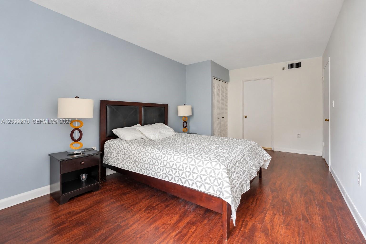 Spacious primary bedroom featuring warm wood flooring, generous closet space, large windows, and a neutral color palette for a comfortable retreat.