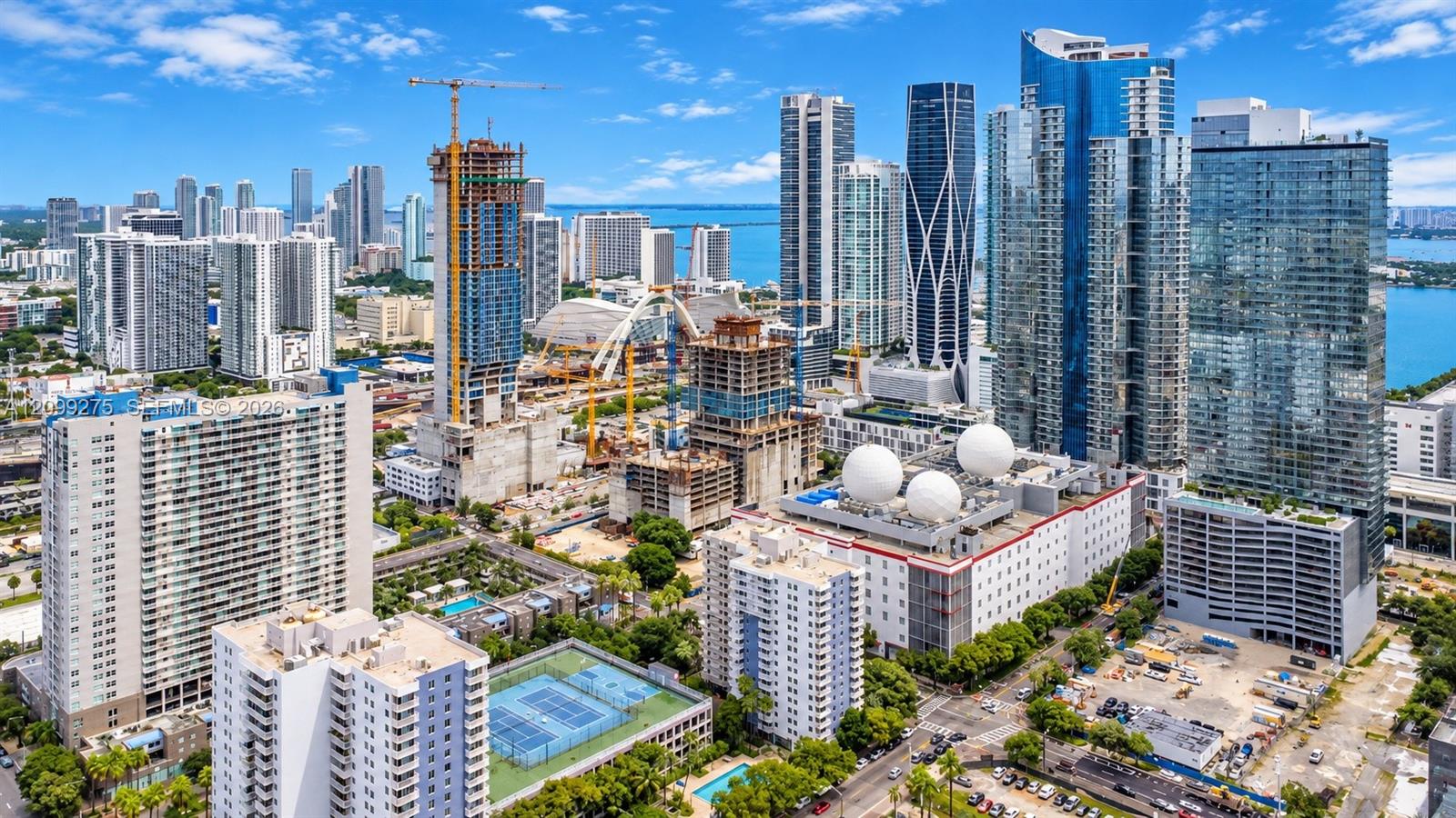 Stunning aerial view of Miamis vibrant skyline, showcasing modern high-rise towers, Biscayne Bay, and ongoing urban development in a dynamic waterfront setting.