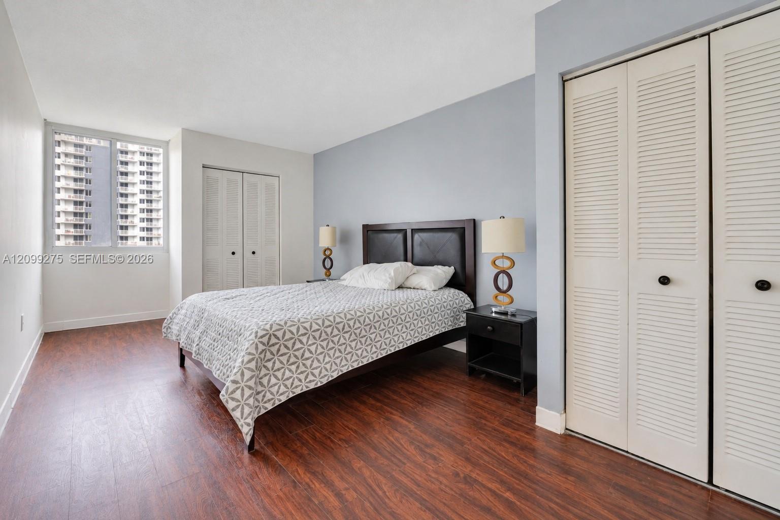 Spacious bedroom featuring elegant wood flooring, a sophisticated upholstered headboard, and ample closet space, creating a refined and inviting retreat.