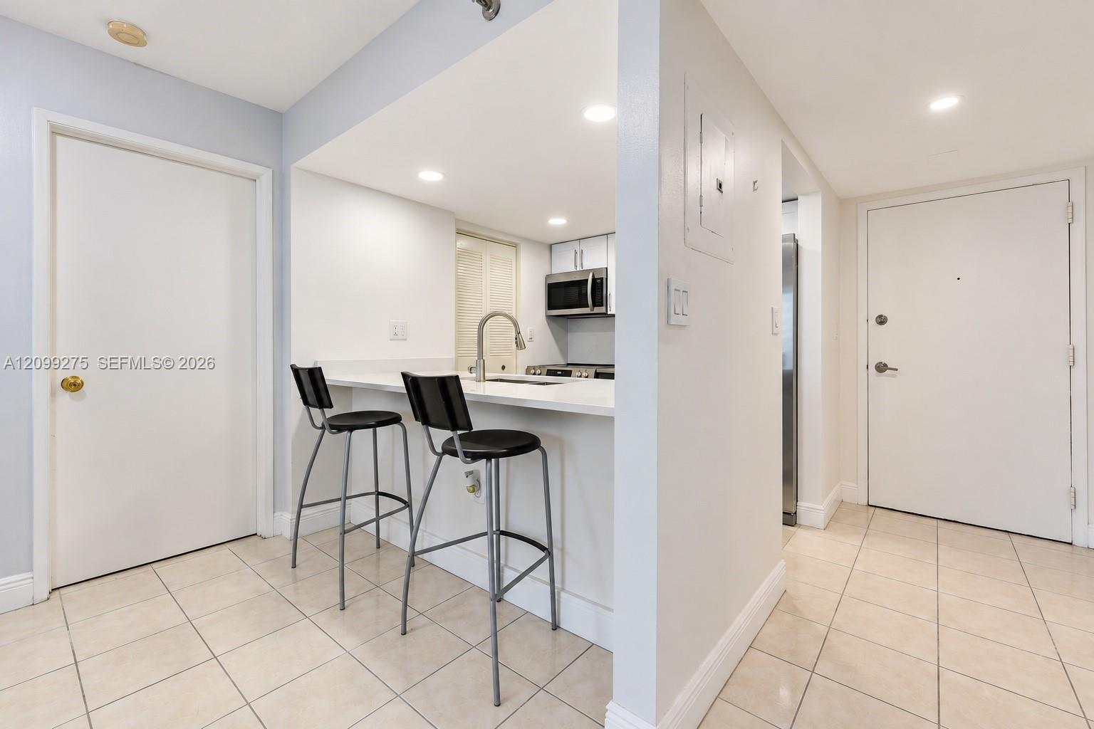 Bright, modern kitchen featuring a sleek breakfast bar with contemporary seating, recessed lighting, and elegant tile flooring, offering a clean and inviting space.