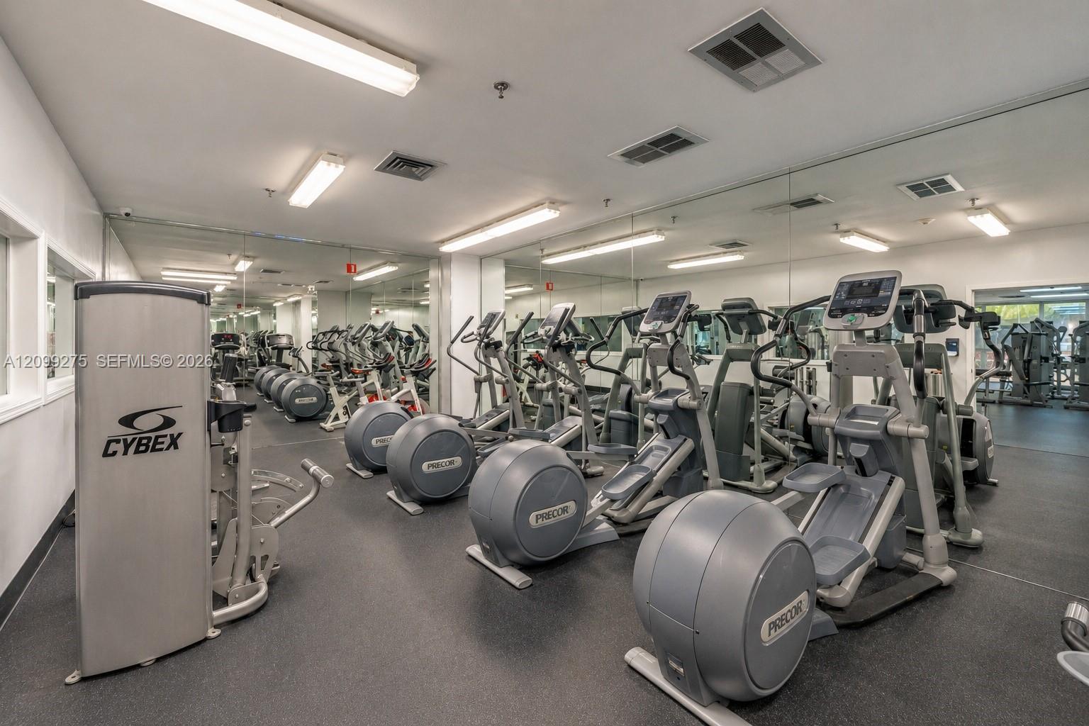 Fully equipped fitness center featuring a wide selection of cardio machines, including elliptical trainers, along with mirrored walls and modern exercise equipment for a convenient indoor workout experience.