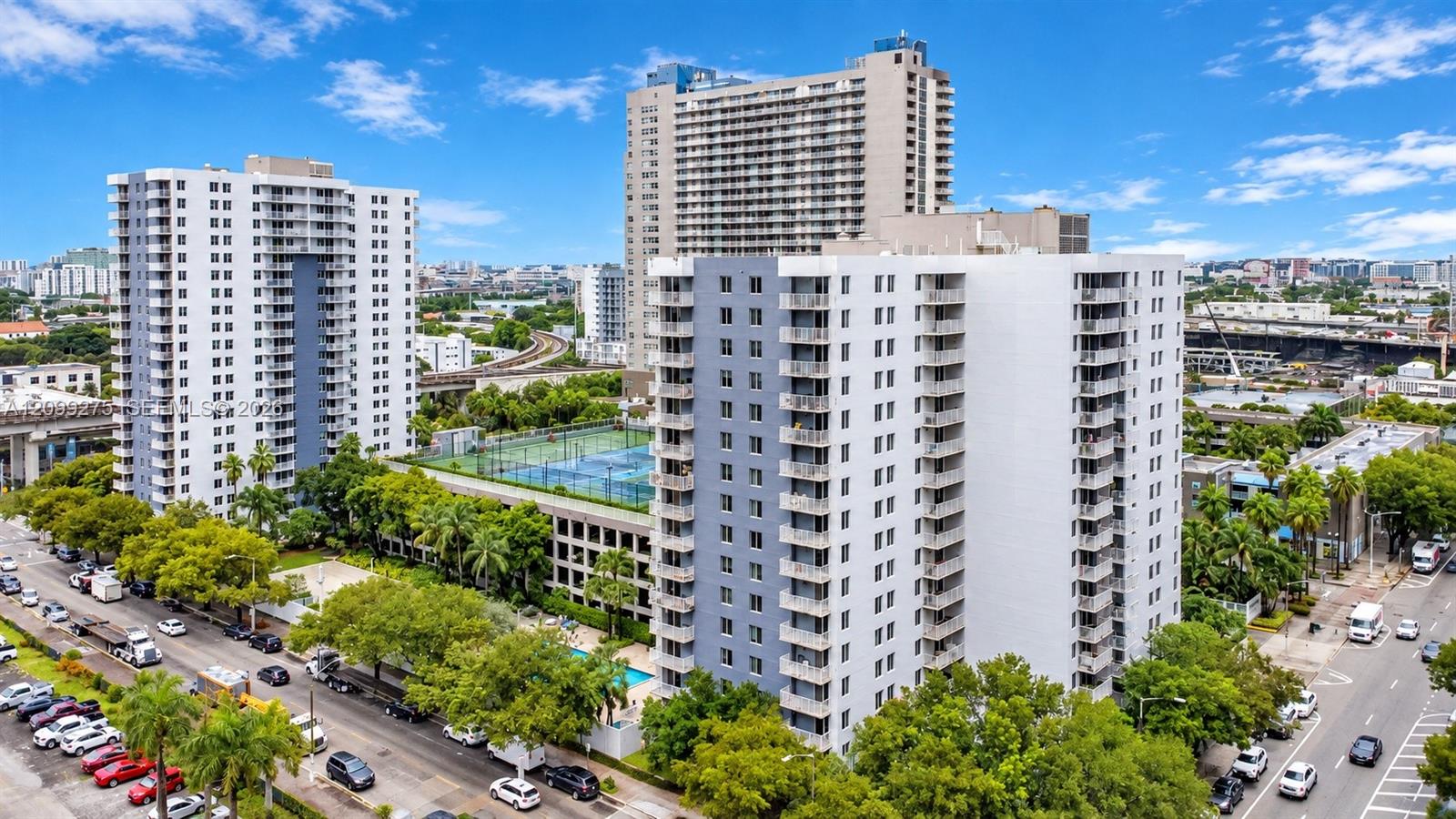 Aerial view of The Madison condominium community, showcasing modern high-rise buildings, lush tropical landscaping, and convenient urban surroundings.