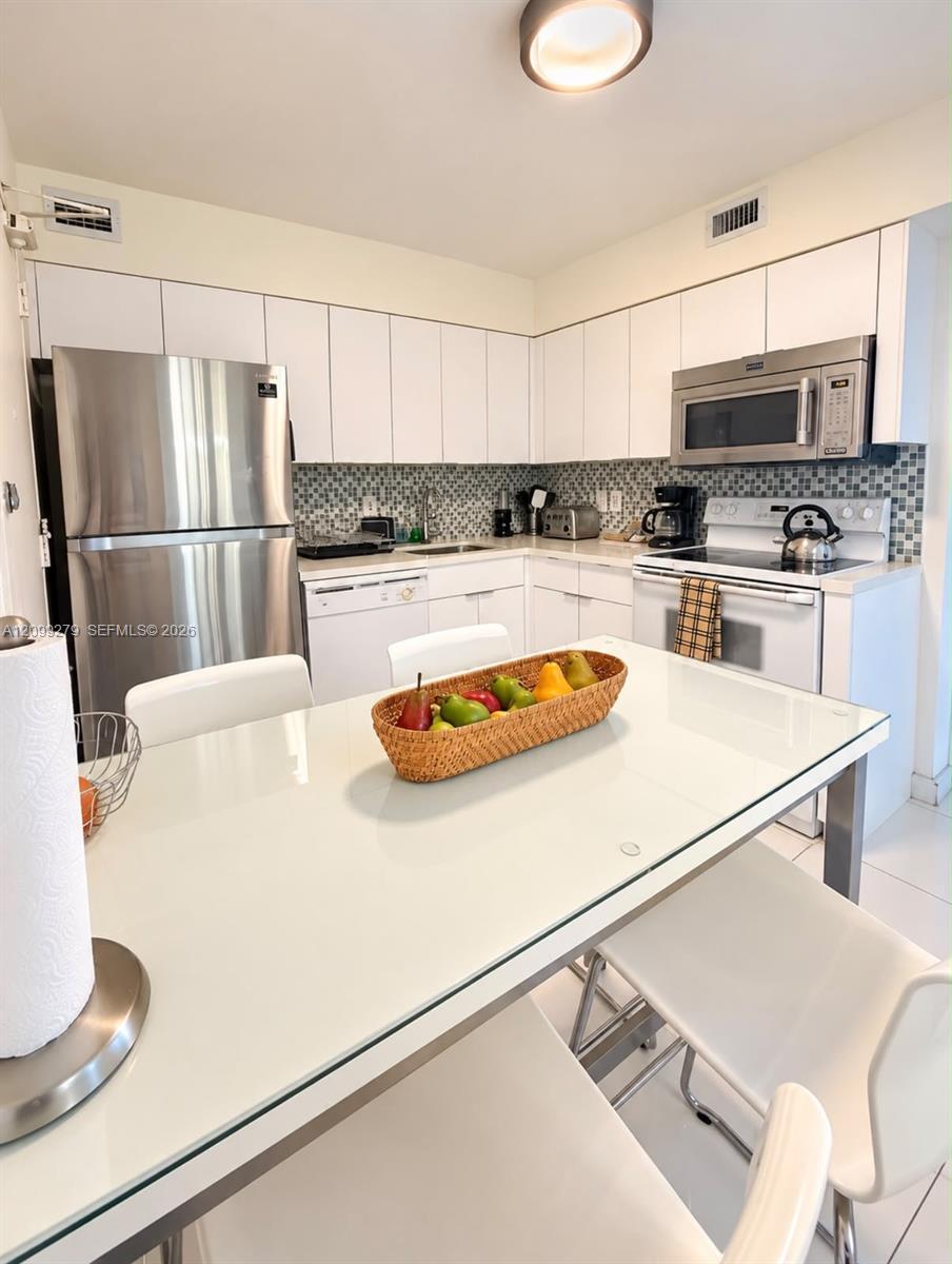 Kitchen featuring white cabinetry, stainless steel appliances, a mosaic tile backsplash, and light-toned tile flooring
