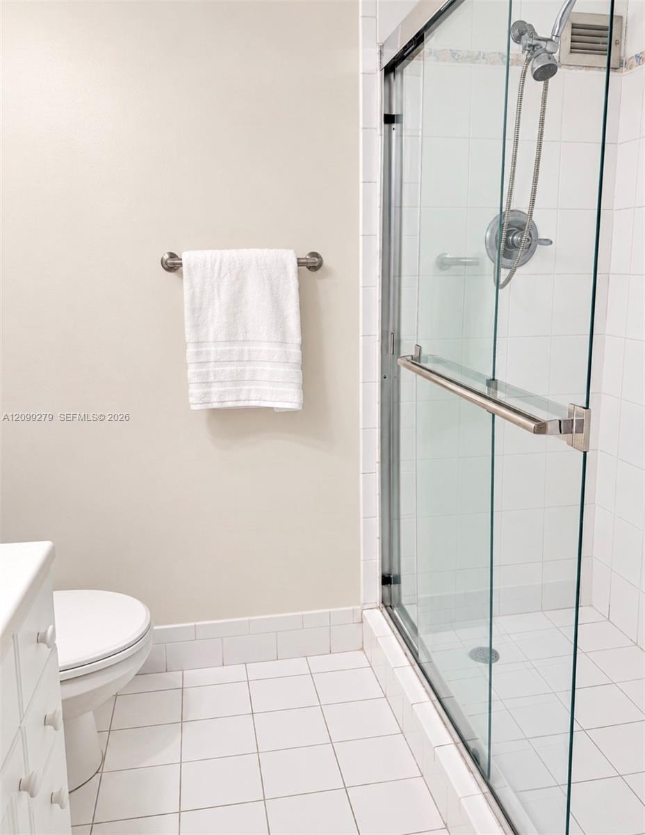 Walk-in shower featuring a frameless glass enclosure, polished metal hardware, and a handheld showerhead, finished with white tile wall and floor surfaces