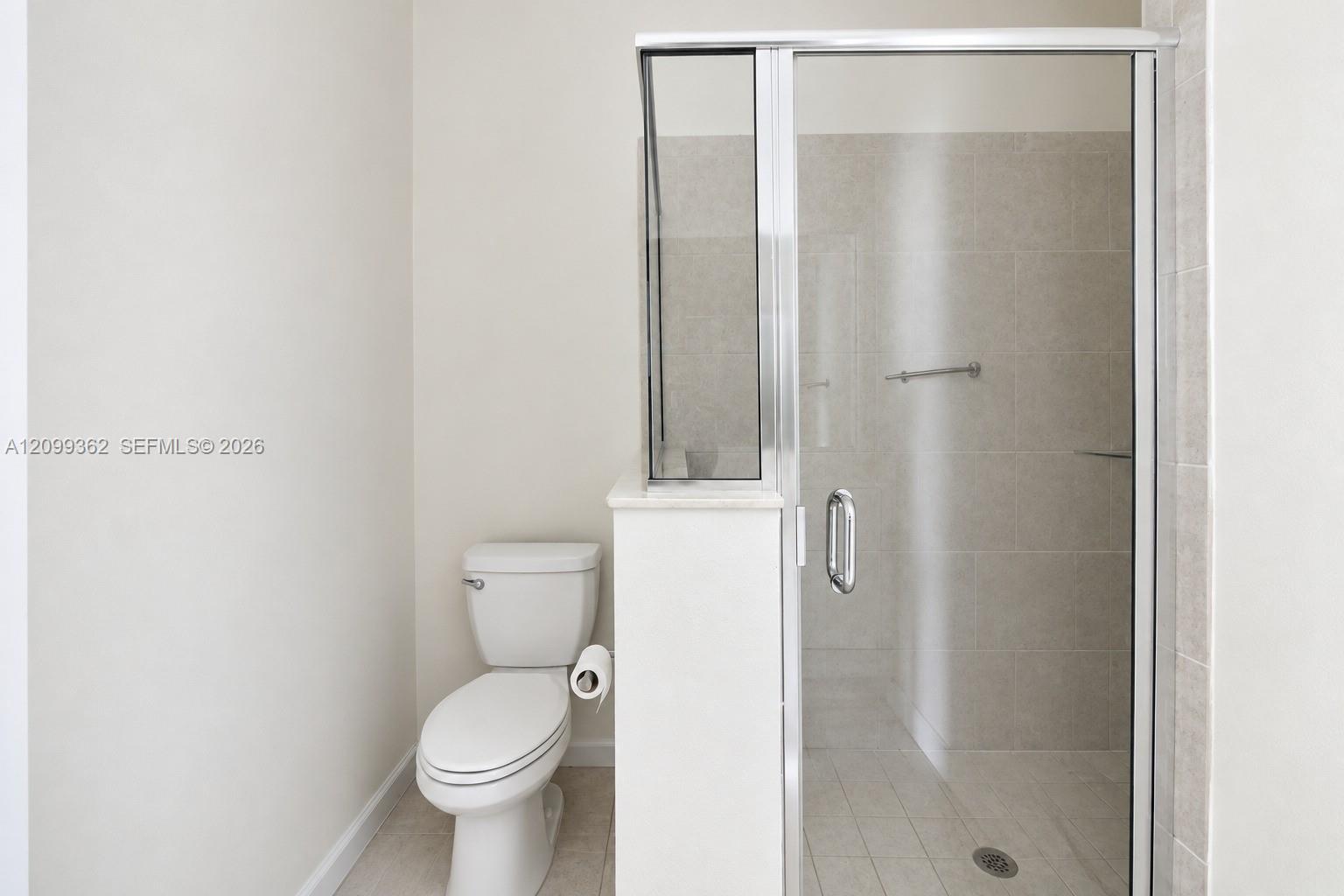 Walk-in shower with a glass enclosure, neutral tile surround, and chrome hardware, paired with a standard-profile toilet