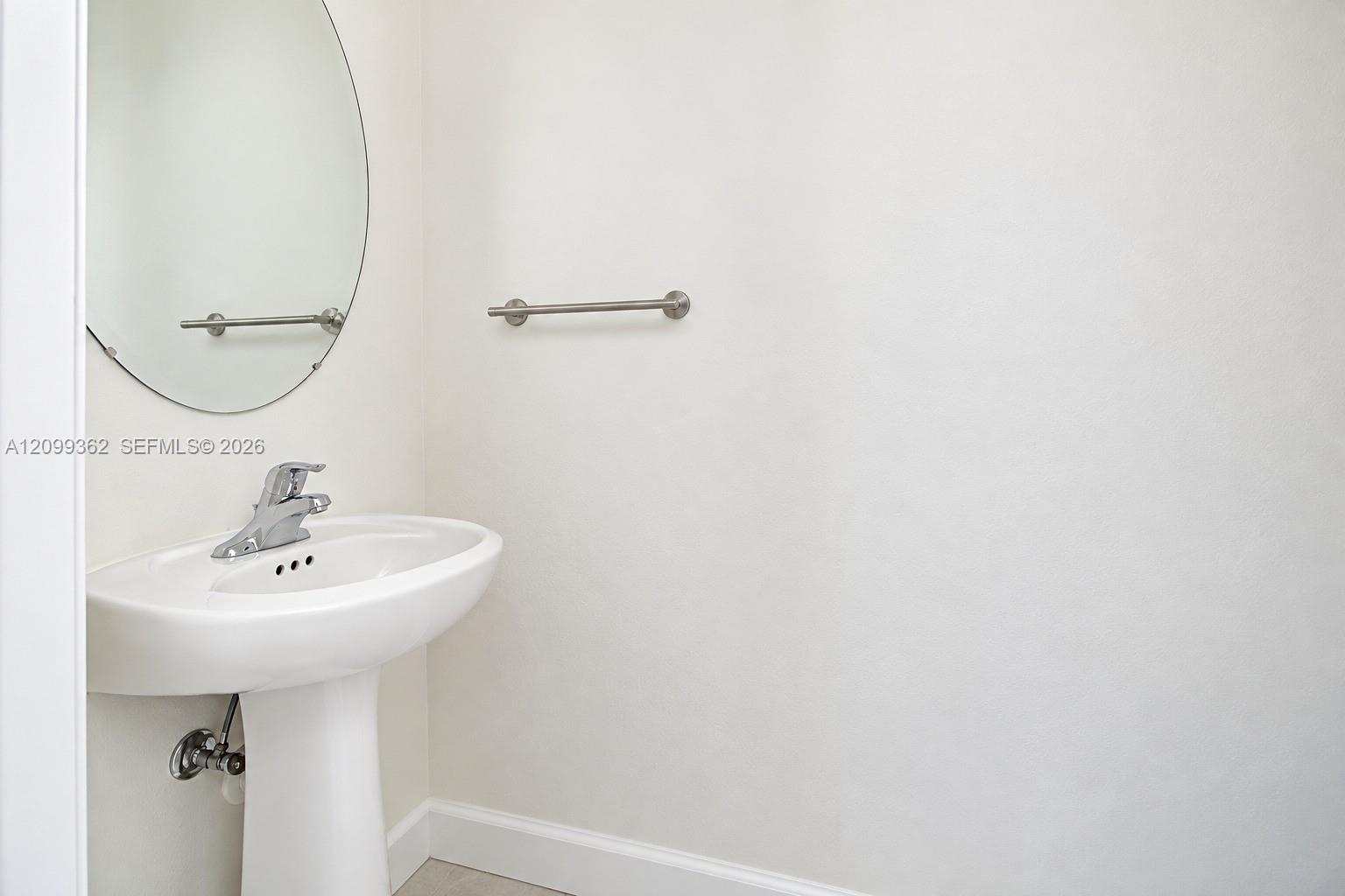 White pedestal sink with a polished chrome faucet, oval frameless wall mirror, and polished chrome towel bar