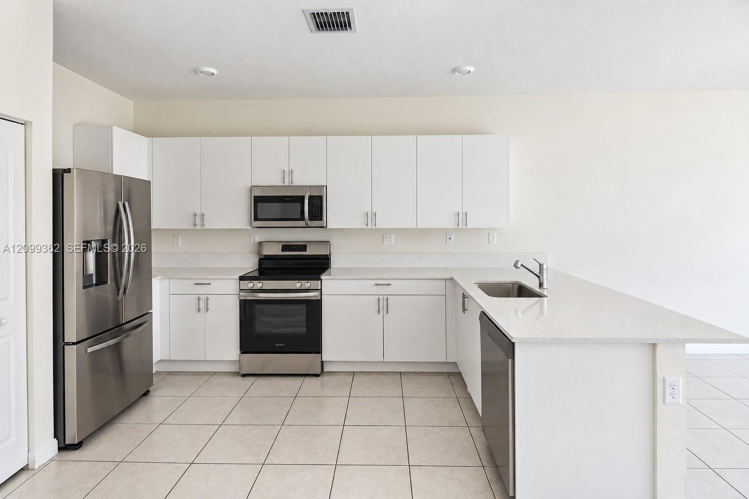 Kitchen featuring white shaker-style cabinetry, solid-surface countertops, stainless steel appliances, a peninsula with an undermount sink, and tiled flooring