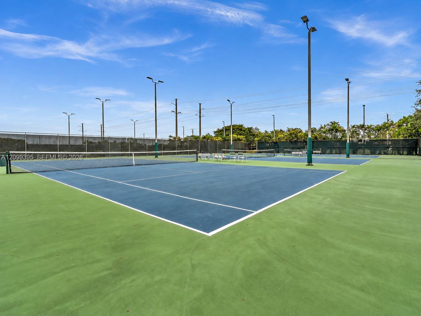 Multiple hard-court tennis surfaces featuring perimeter fencing, integrated lighting poles, and dark-toned court surfacing