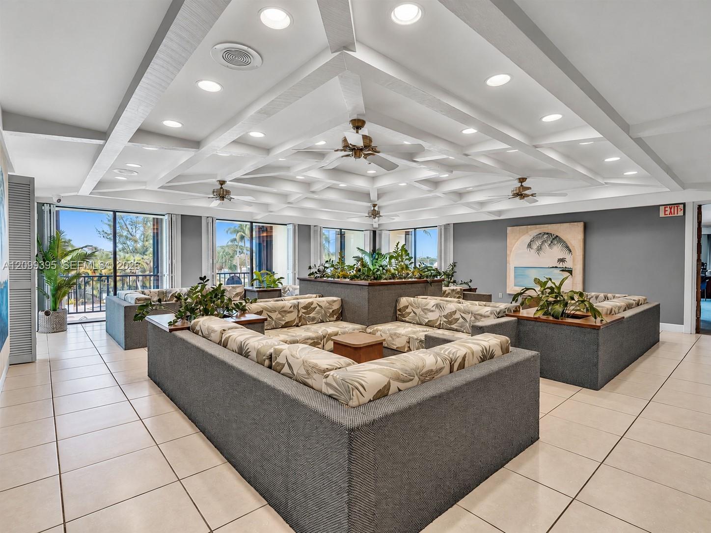 Expansive common area featuring a coffered ceiling, recessed lighting, ceiling fans, tile flooring, and large glass sliding doors