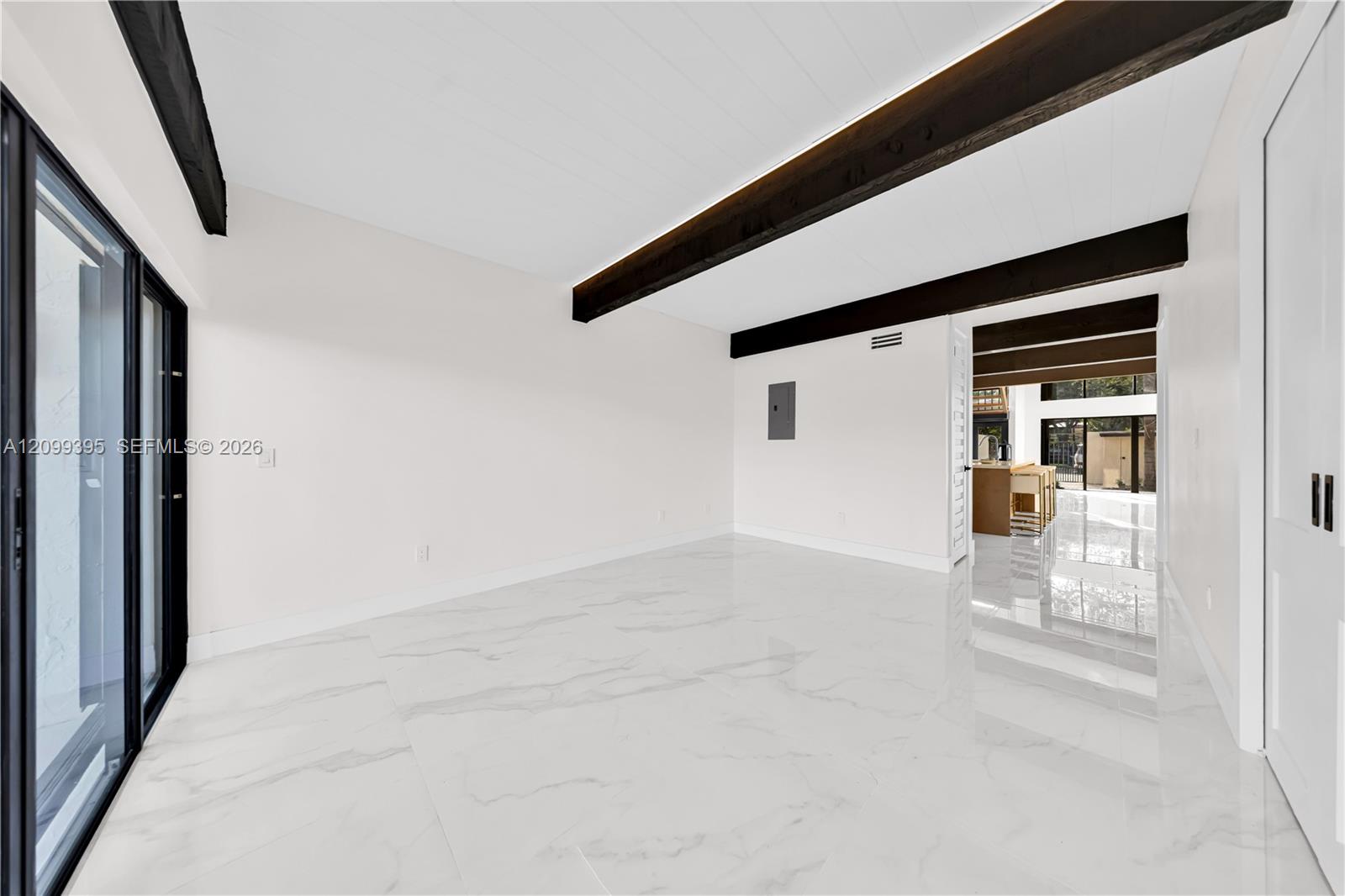 Polished stone-finish flooring, exposed structural ceiling beams, and floor-to-ceiling glass sliding doors with black frames