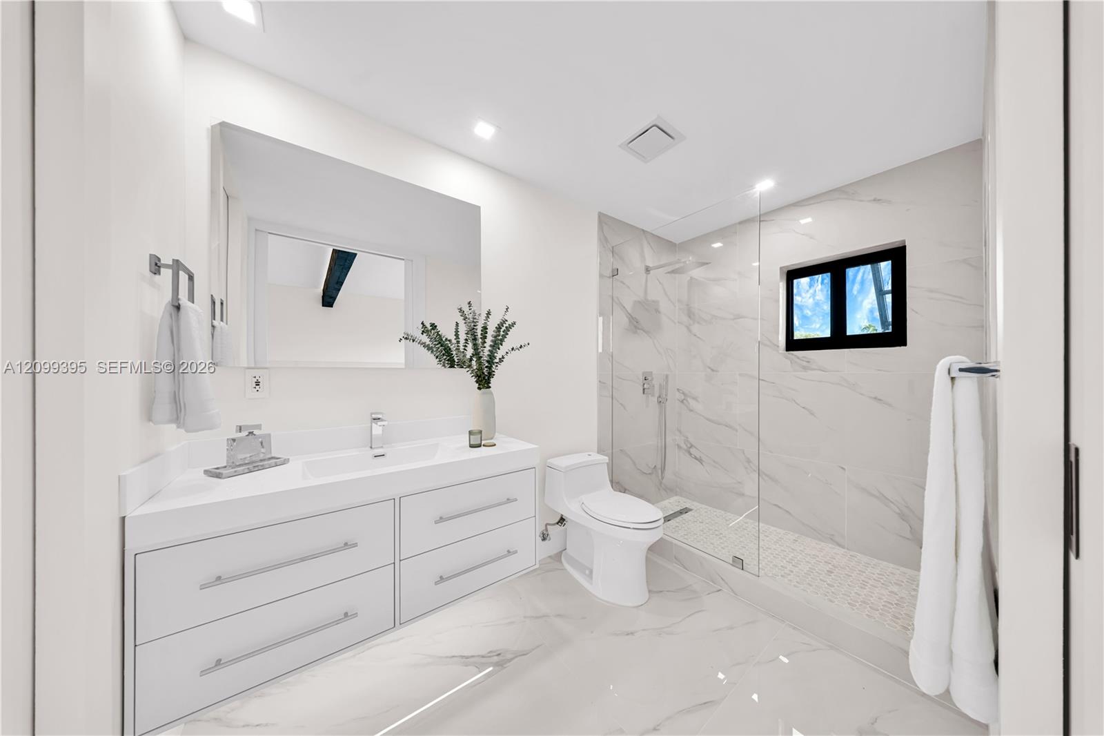 Bathroom featuring a white floating dual-drawer vanity with an integrated sink, floor-to-ceiling stone-style tile shower surround with a glass enclosure, and stone-style flooring