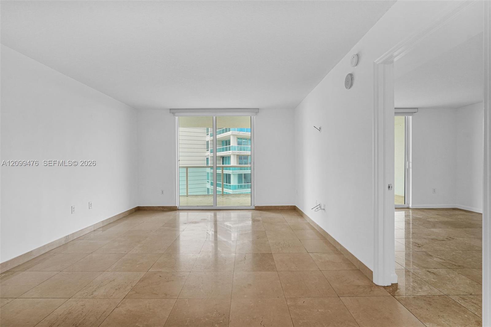 Spacious interior featuring large-format stone-finish tile flooring, white walls, and a sliding glass door providing external access