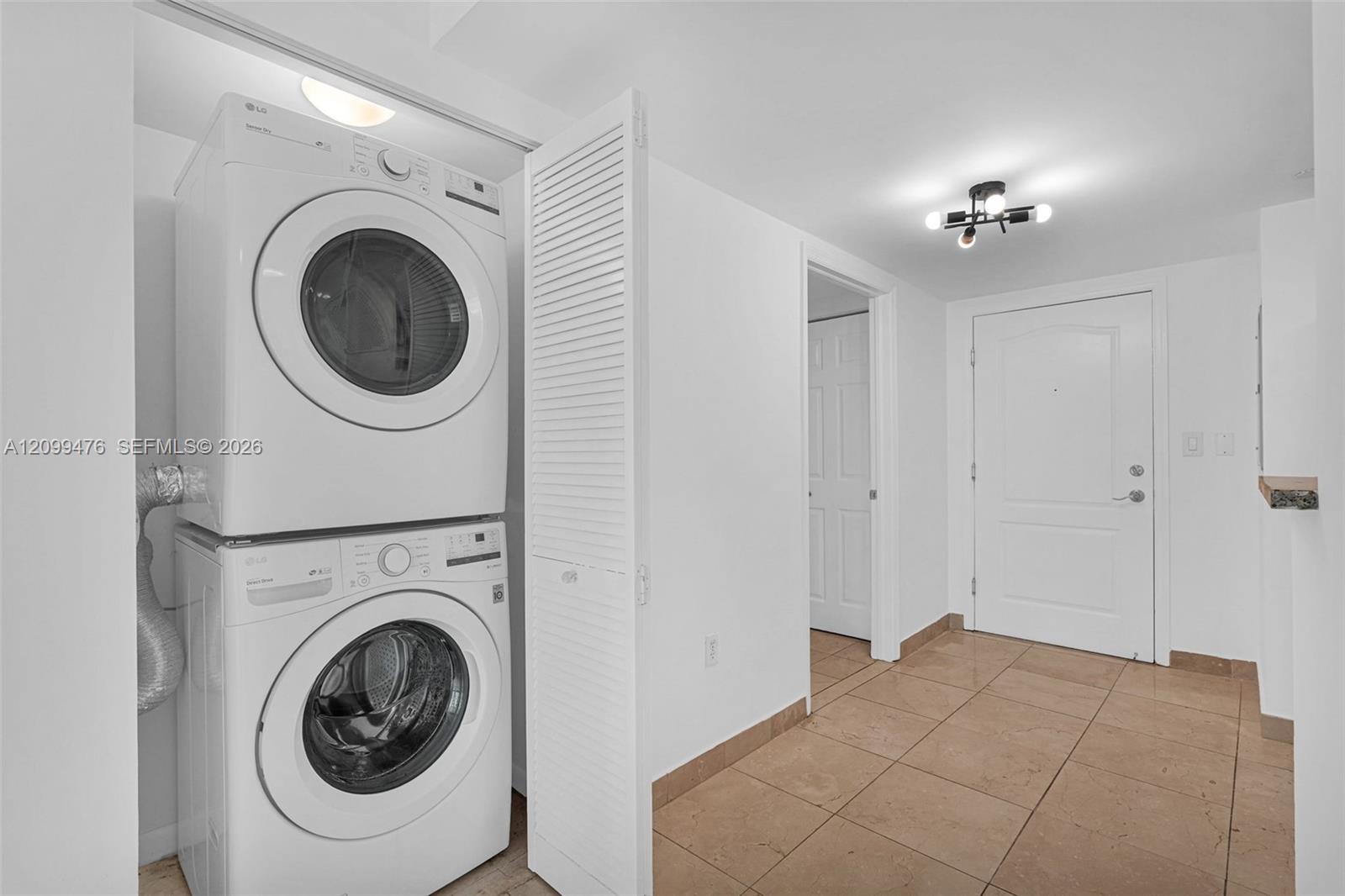Stacked laundry center with white louvered door, tile flooring, and multi-light flush mount ceiling fixture