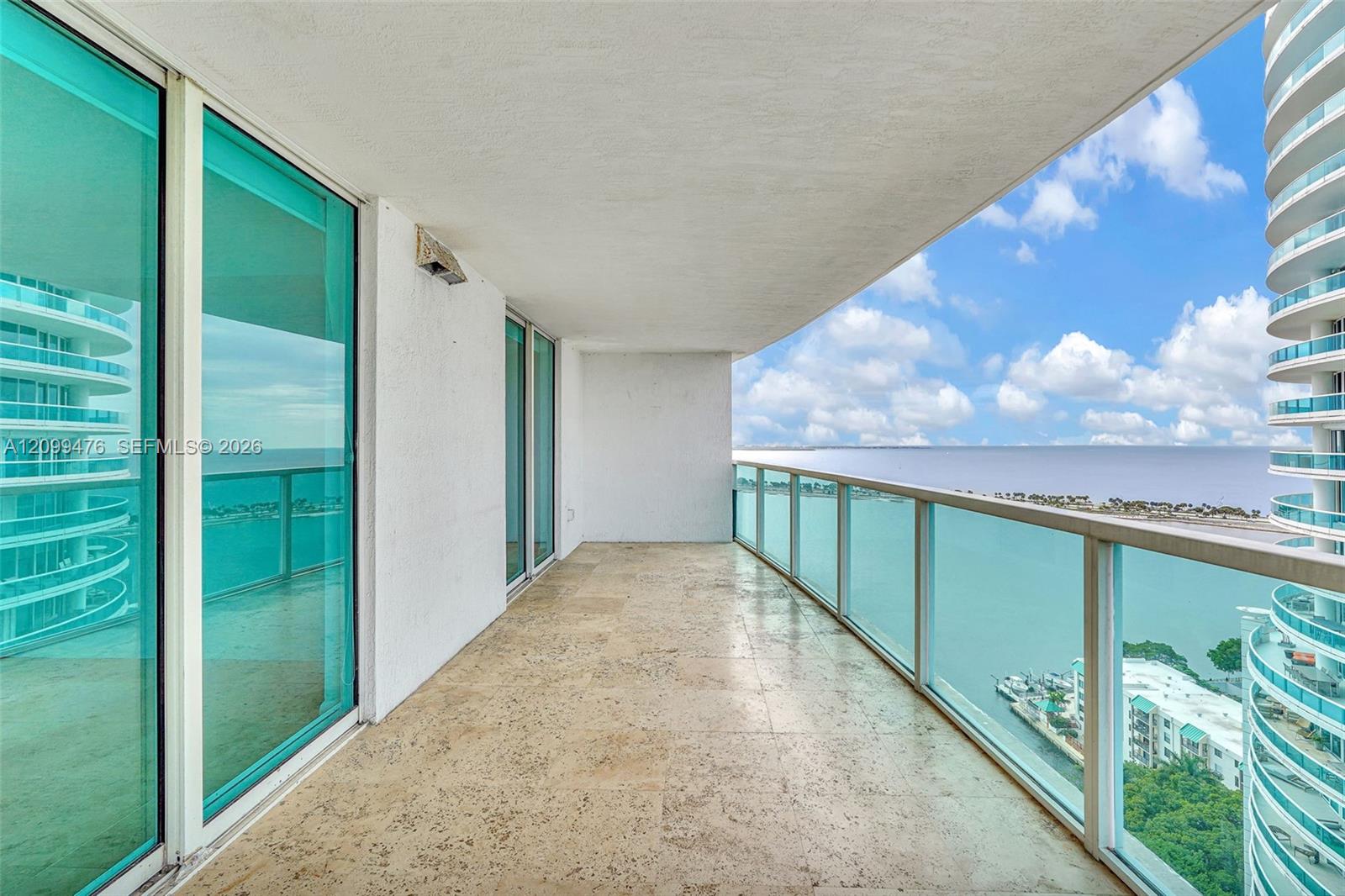 Covered balcony featuring stone tile flooring and a glass panel railing overlooking water