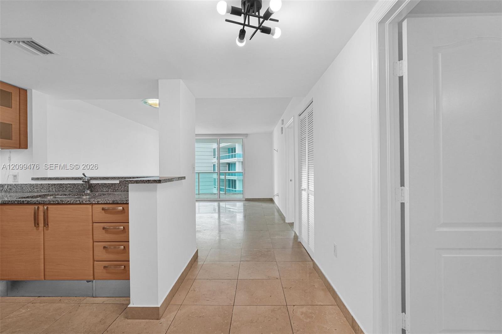 Kitchen featuring wood-finish cabinetry, stone-surfaced countertops, neutral tile flooring, louvered closet doors, and a multi-bulb geometric light fixture