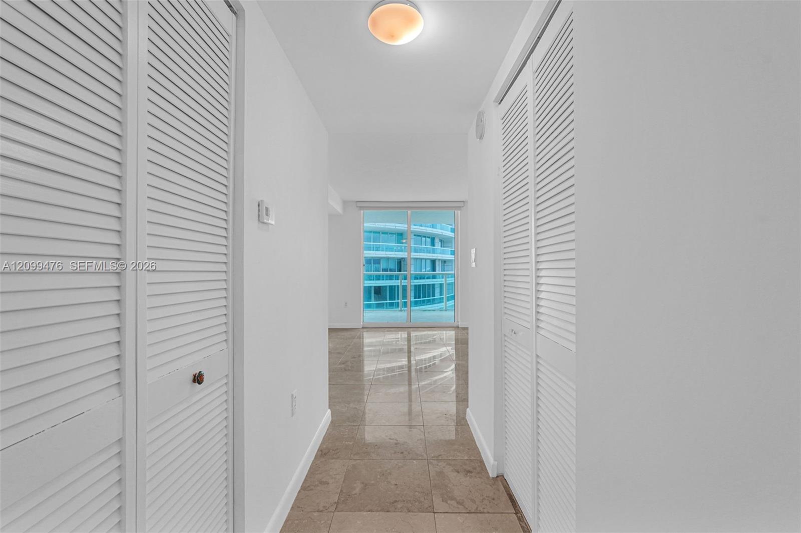 Hallway featuring polished tile flooring, dual floor-to-ceiling closets with white louvered doors, and a flush-mount dome light fixture