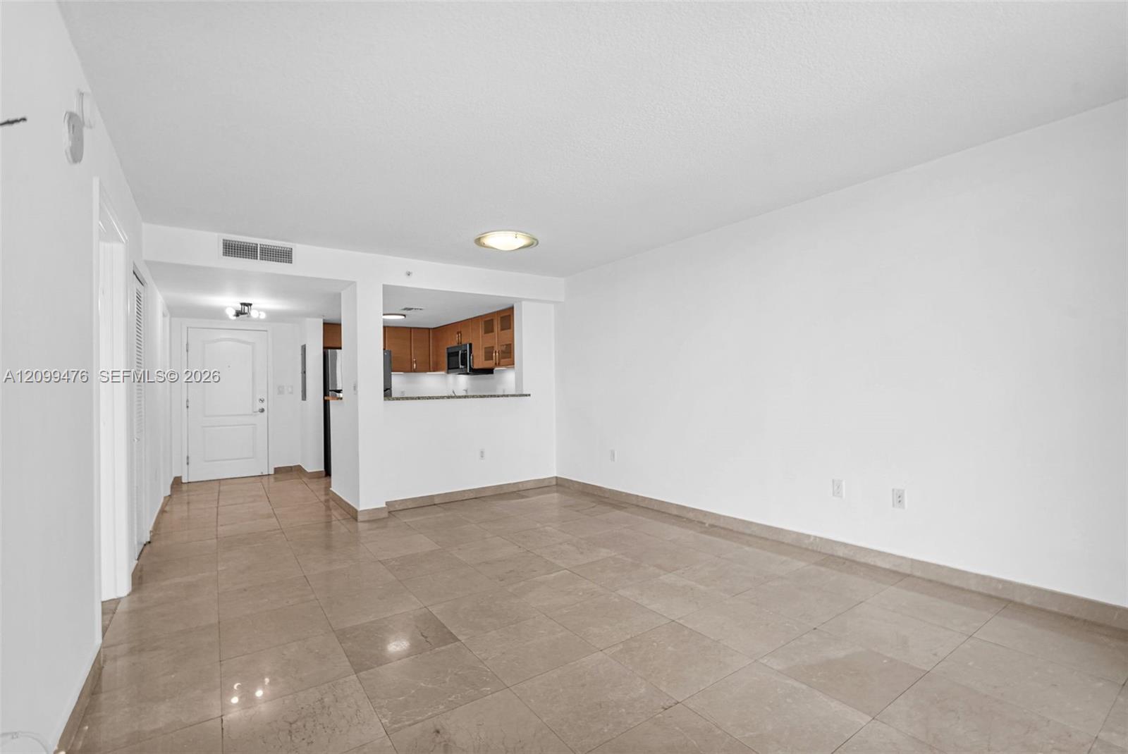 Open-concept interior featuring large-format stone tile flooring, smooth ceilings, recessed lighting, and a breakfast bar pass-through to the kitchen with wood cabinetry