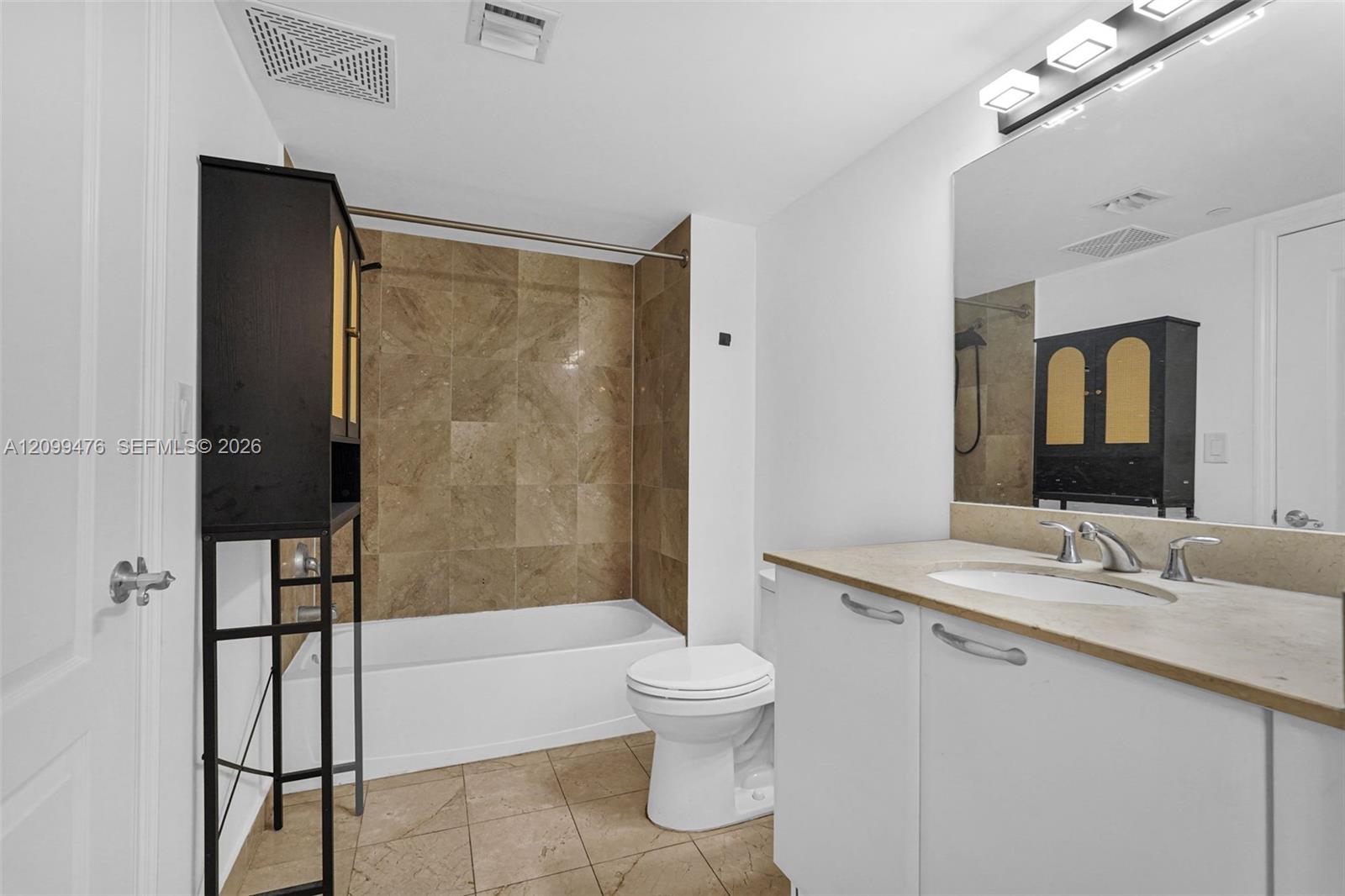 Bathroom featuring a stone-tile bathtub surround, neutral-toned floor tile, a white cabinet vanity with a stone countertop, an integrated oval sink, and a multi-light vanity fixture