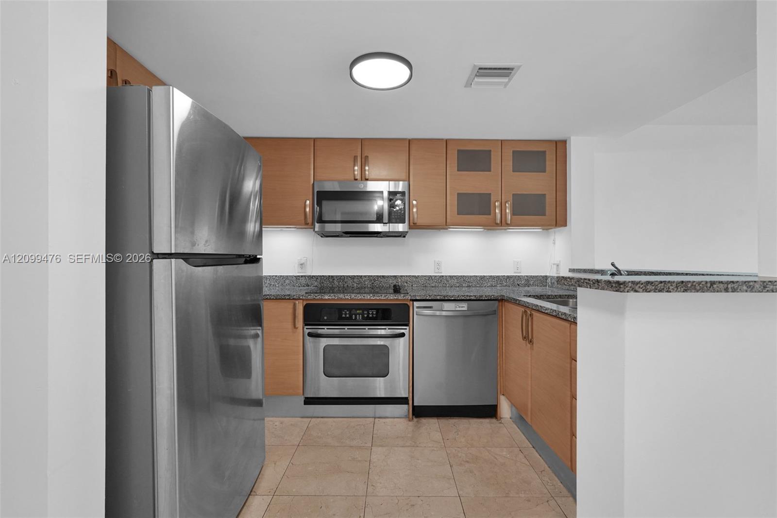 Kitchen featuring flat-panel wood cabinetry, speckled stone countertops, stainless steel appliances, and tile flooring
