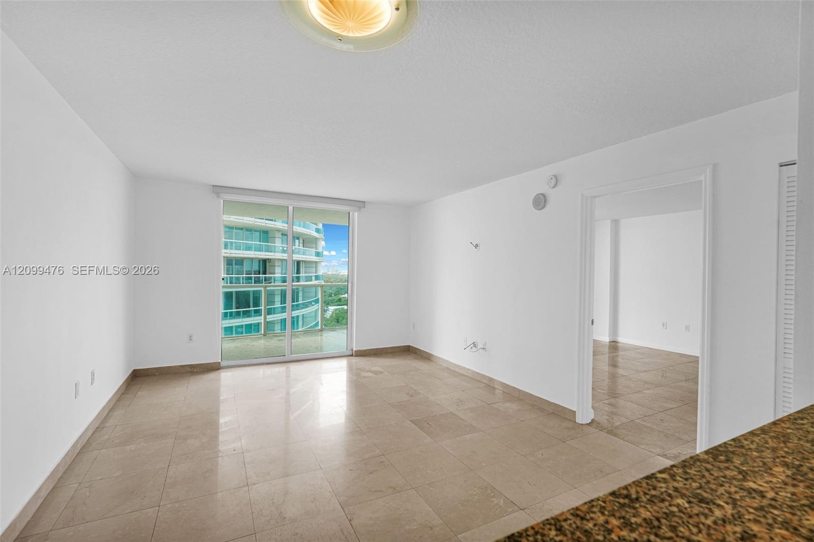 Open-concept interior featuring large-format stone flooring, floor-to-ceiling glass sliding doors, and neutral wall tones
