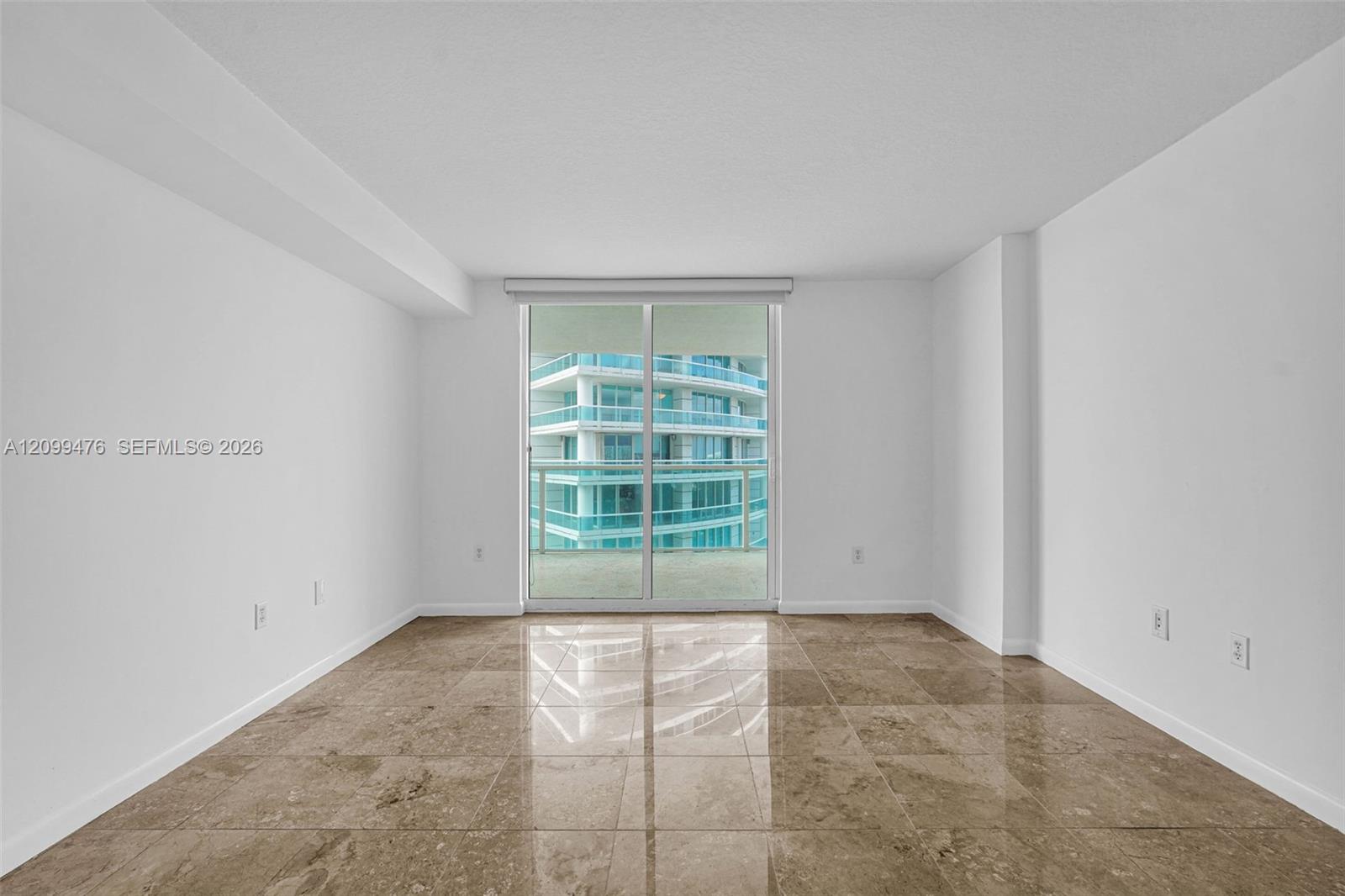 Expansive interior space featuring large-format polished stone flooring, high ceilings, and floor-to-ceiling glass sliding doors opening to a balcony