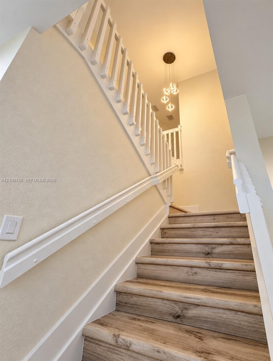 Staircase featuring wood-finish treads, white railings, and a multi-pendant light fixture