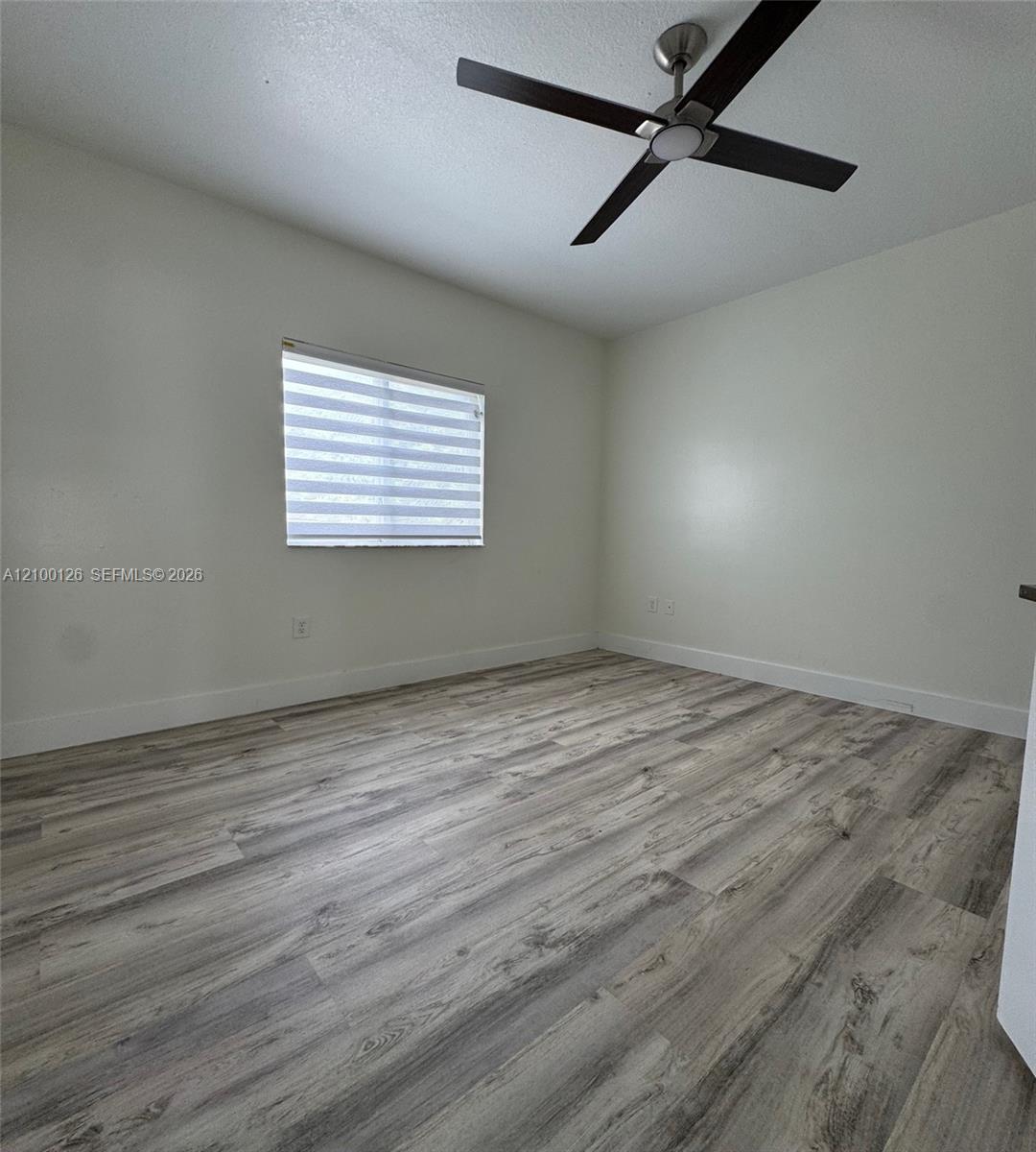 Interior space featuring wood-finish flooring, neutral walls, a modern ceiling fan with integrated lighting, and a window equipped with horizontal roller shades