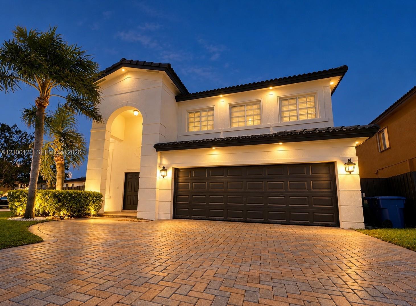 Stucco exterior with an arched entryway, paver driveway, dark-toned multi-panel garage door, and low-profile tile roofing