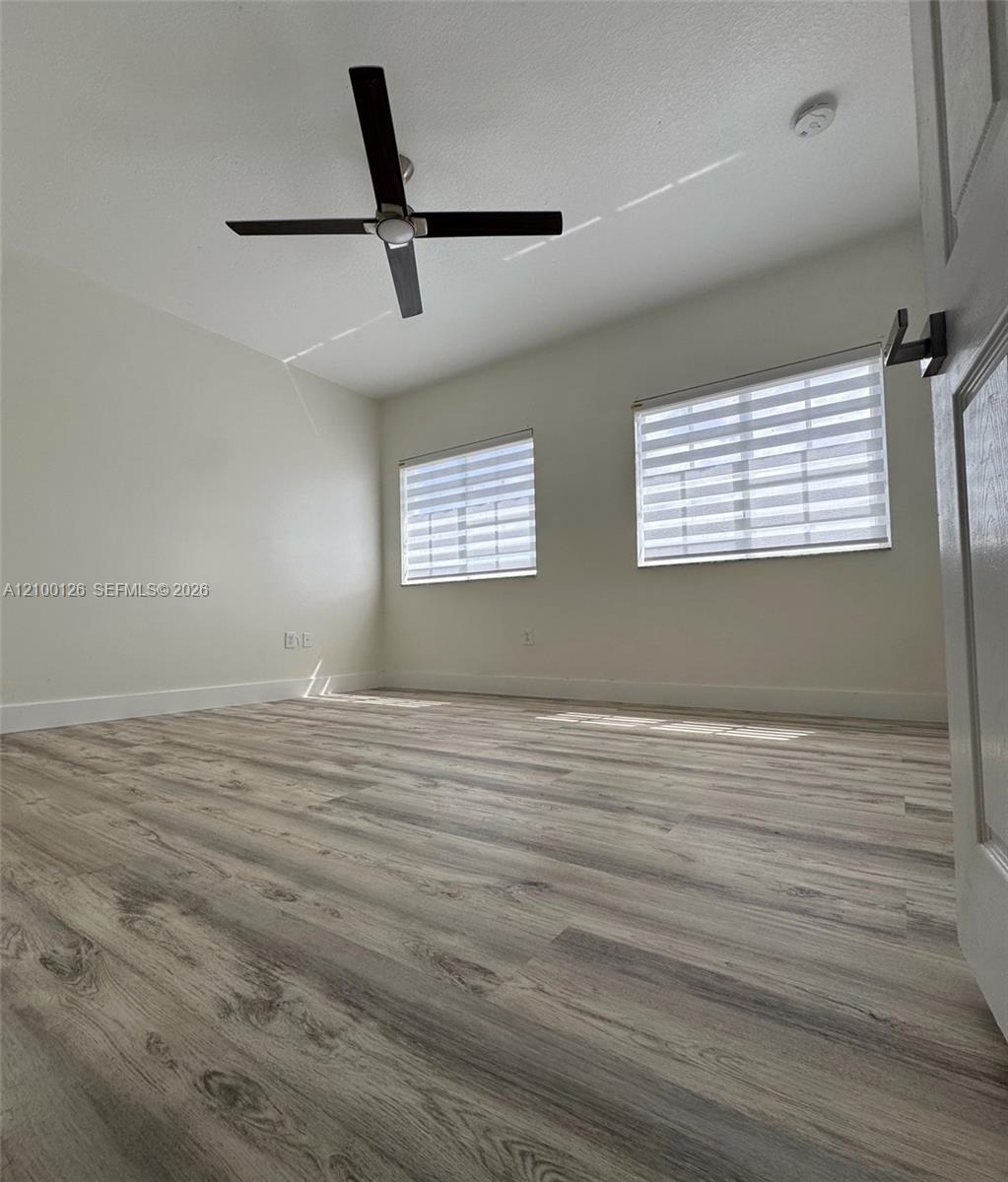 Interior room featuring wood-finish flooring, a four-blade ceiling fan, and dual windows equipped with horizontal privacy blinds