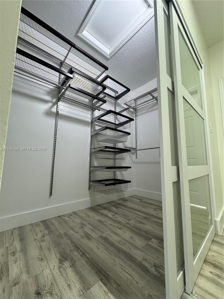 Walk-in closet featuring wood-finish flooring, a white sliding glass-panel door, and a custom wire shelving system with integrated pull-out drawers