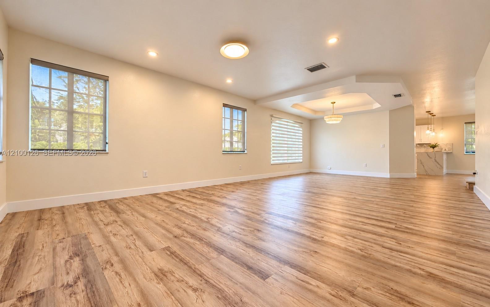 Open-concept interior featuring wood-finish flooring, tray ceiling with recessed lighting, multi-pane windows, and a suspended chandelier