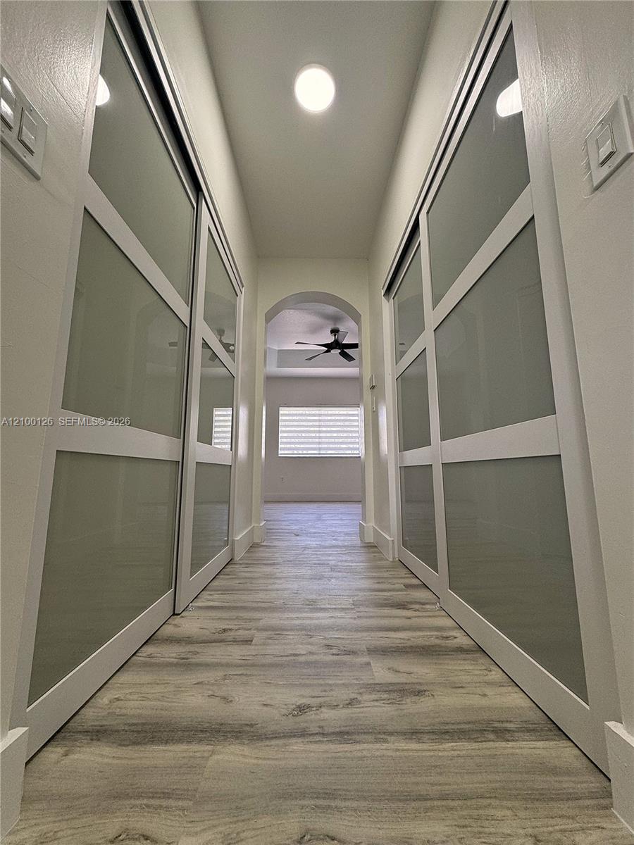 Hallway featuring wood-finish flooring, dual sliding closet doors with frosted glass panels, and an arched architectural opening