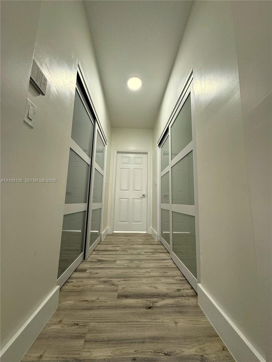 Hallway featuring wood-finish flooring, two sets of sliding closet doors with frosted glass panels, and a paneled interior door with metal hardware
