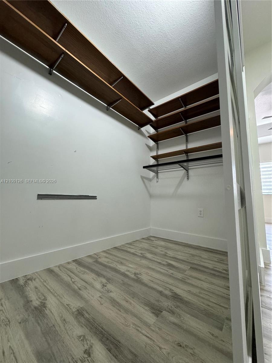 Walk-in closet featuring wood-finish flooring and tiered, built-in shelving with integrated clothing rods