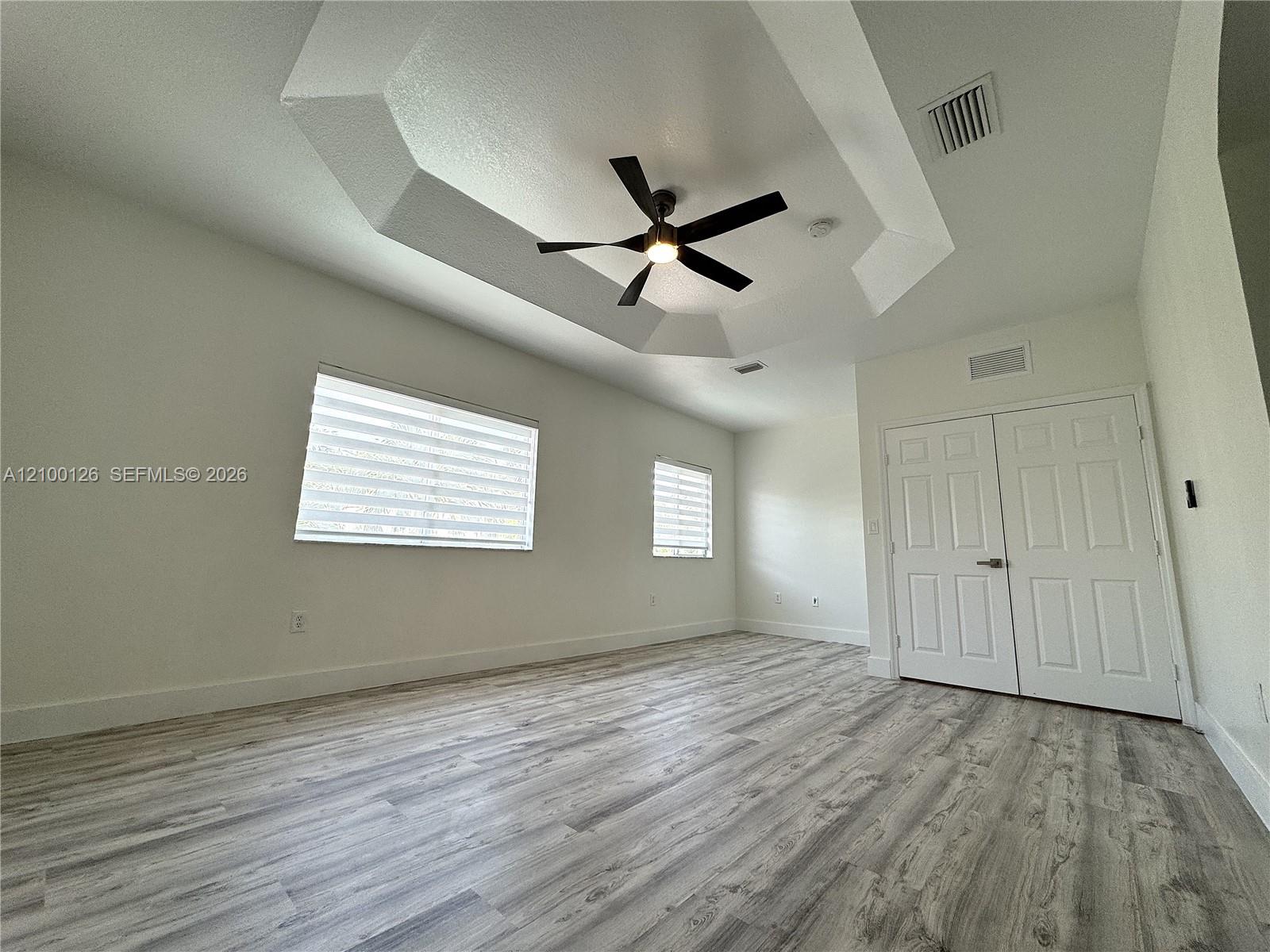 Tray ceiling with an integrated light-fixture ceiling fan, wood-finish flooring, and double-panel doors