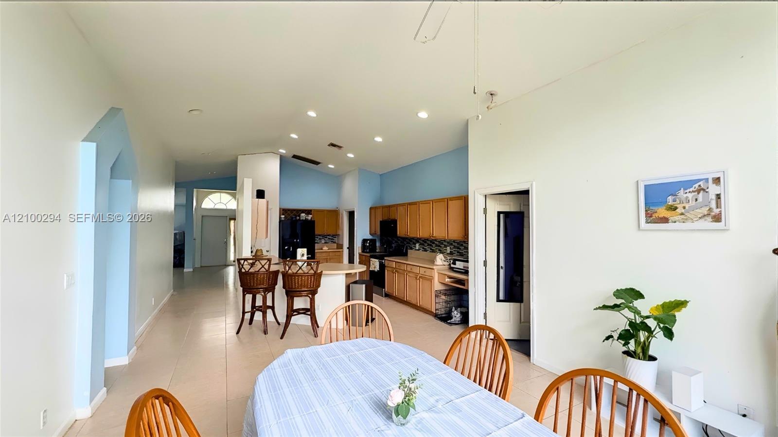 Open-concept interior featuring vaulted ceilings recessed lighting, tile flooring, and a kitchen equipped with wood cabinetry and a peninsula counter Open-concept interior featuring vaulted ceilings recessed lighting, tile flooring, and a kitchen equipped with wood cabinetry and a peninsula counter