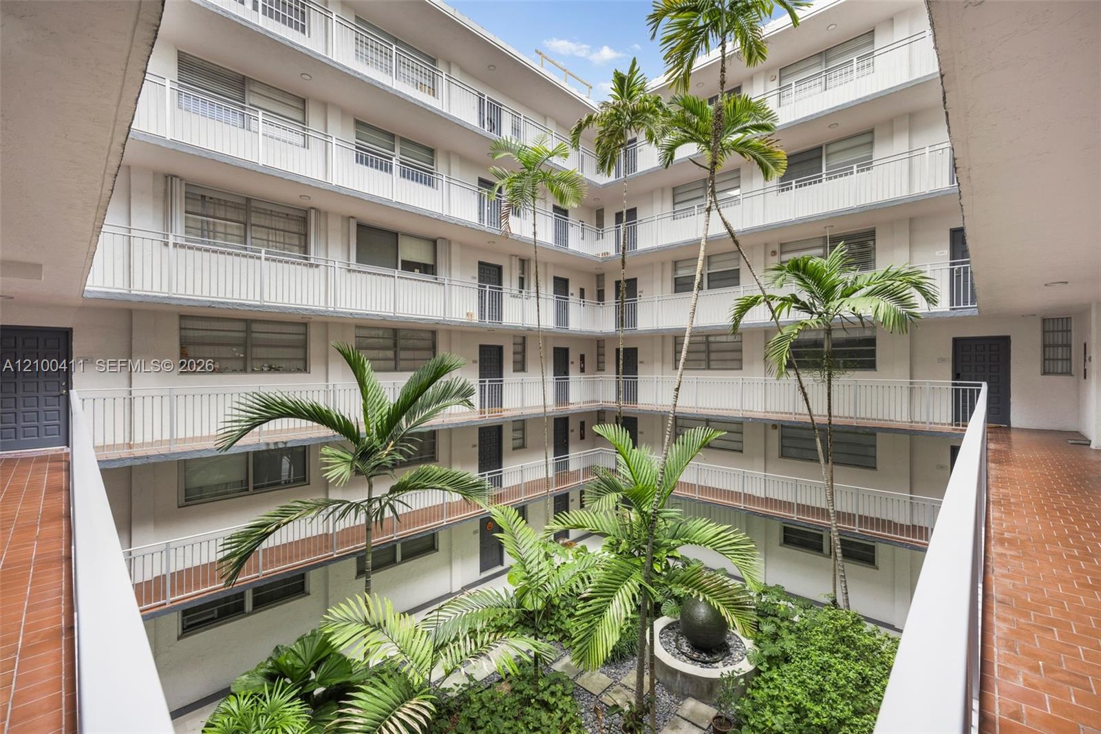 Multi-level open-air central courtyard featuring tile flooring, metal railings, mature palm trees, and a decorative stone fountain