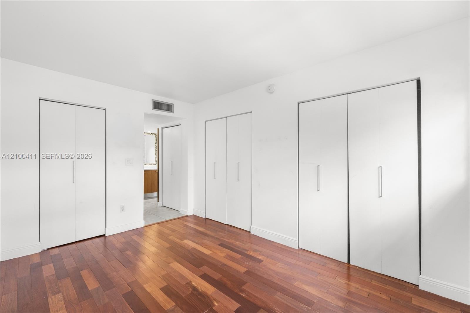 Wood-finish flooring and multiple built-in floor-to-ceiling closets with white panel doors and vertical silver pulls