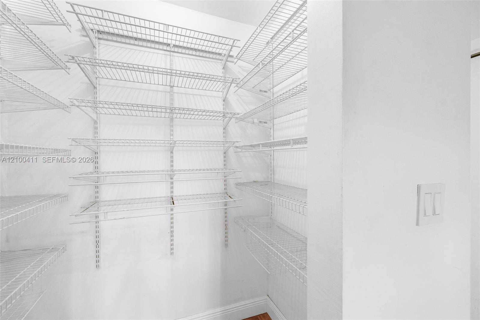 Storage space featuring adjustable white wire shelving units mounted on walls and a dual-switch light fixture