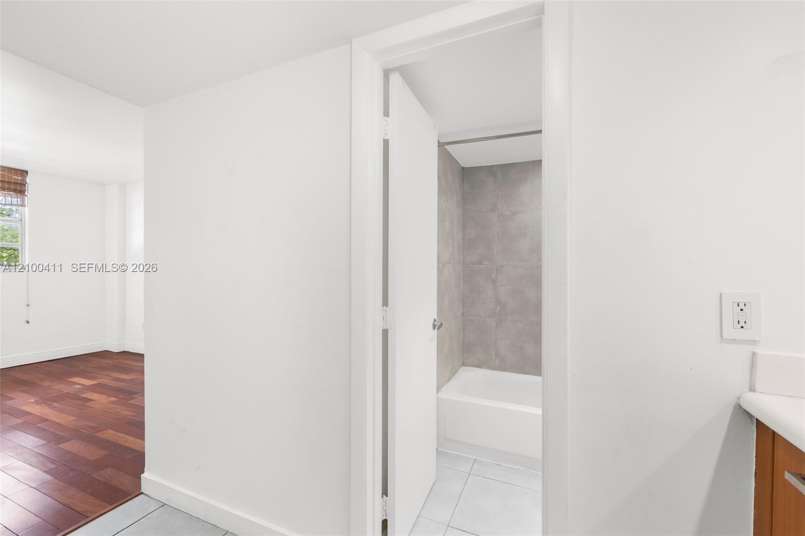 Wood-finish flooring, white walls, and a bathroom featuring a white porcelain tub with grey wall tiling